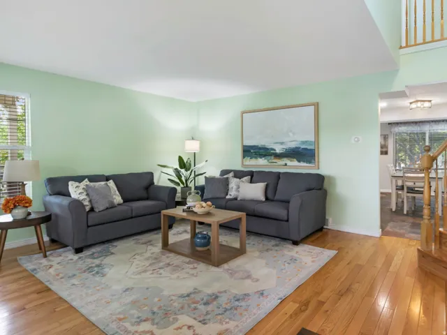 Living area featuring hardwood flooring, a recessed window, light green walls, a two-story ceiling, and a wooden staircase with balusters