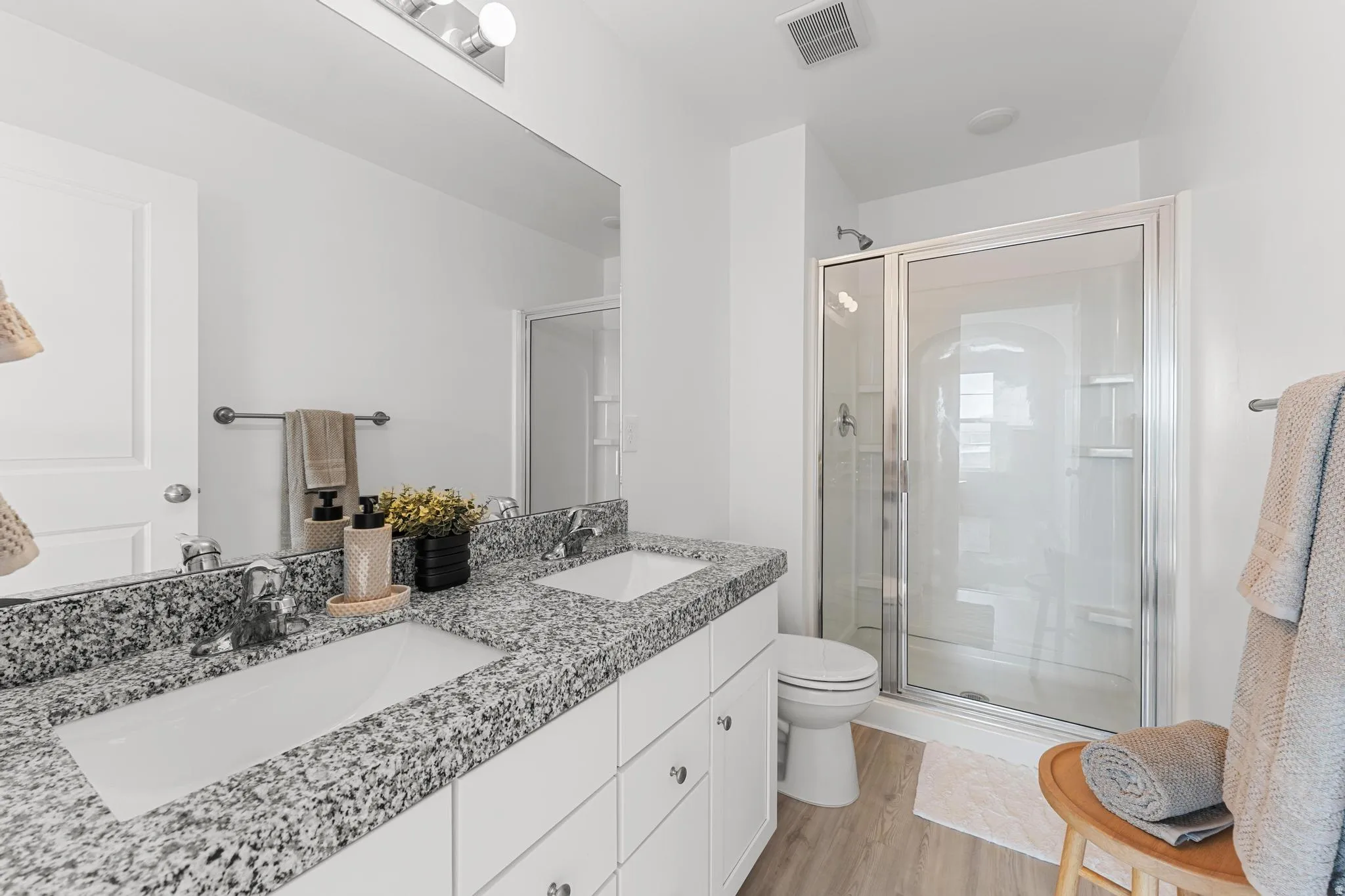 Bathroom featuring a shower stall, double vanity, and light wood-style floors