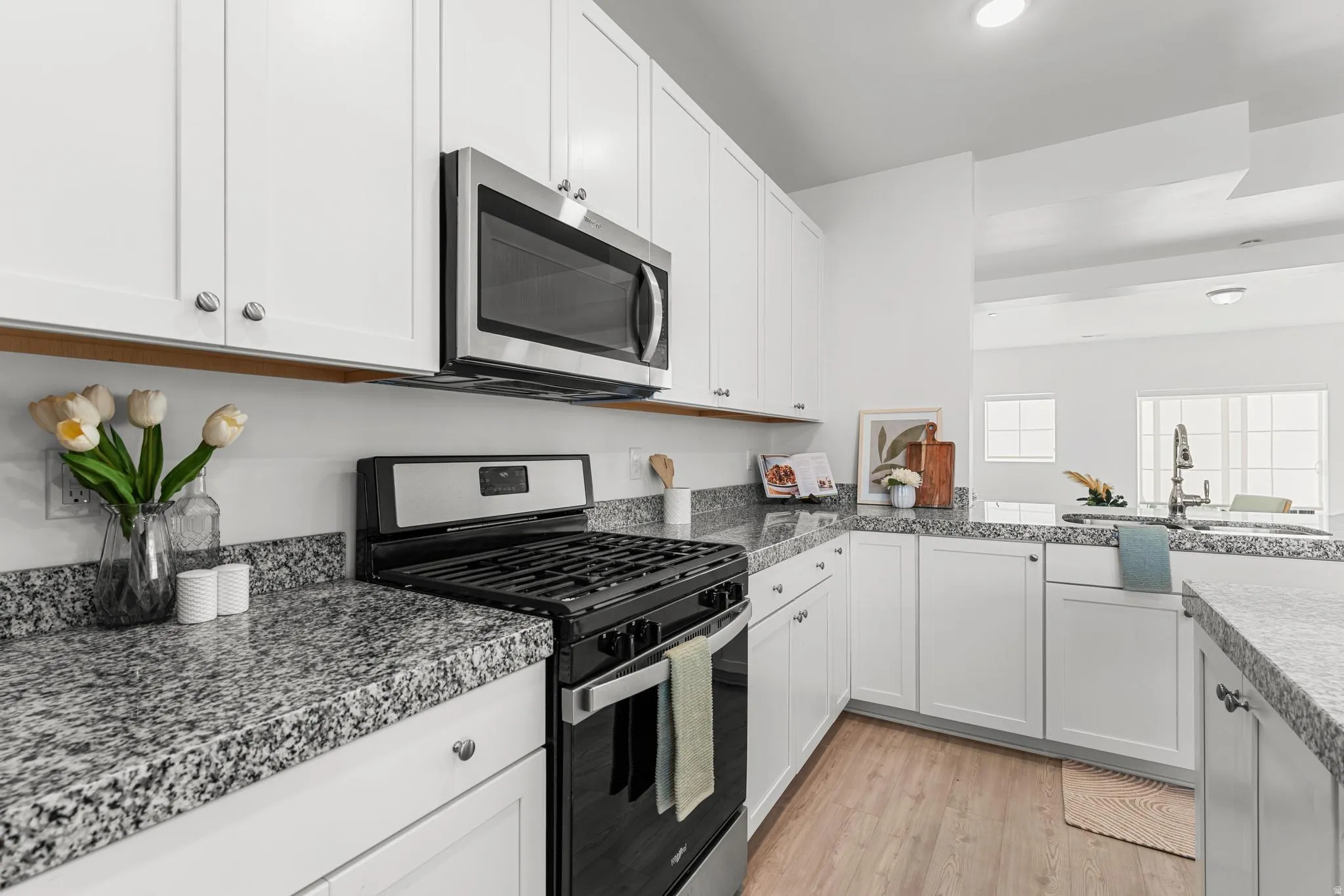 Kitchen featuring stainless steel appliances, white cabinets, light wood finished floors, and dark countertops