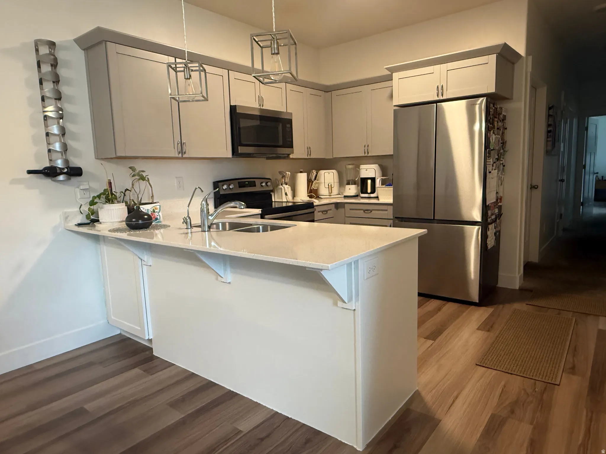 Kitchen featuring a breakfast bar, stainless steel appliances, a peninsula, hanging light fixtures, and dark wood-type flooring