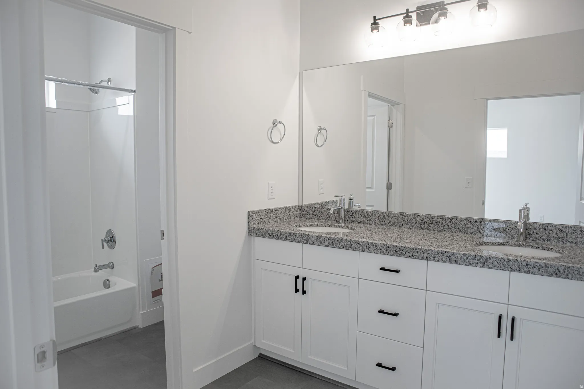 Primary bathroom with dual sinks, painted white wood cabinets and granite countertops.
