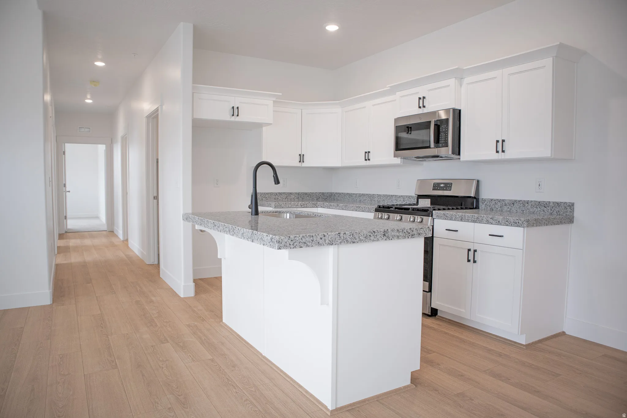 Kitchen with white painted wood cabinets, granite slab countertops, gas range, microwave, dishwasher and disposal.