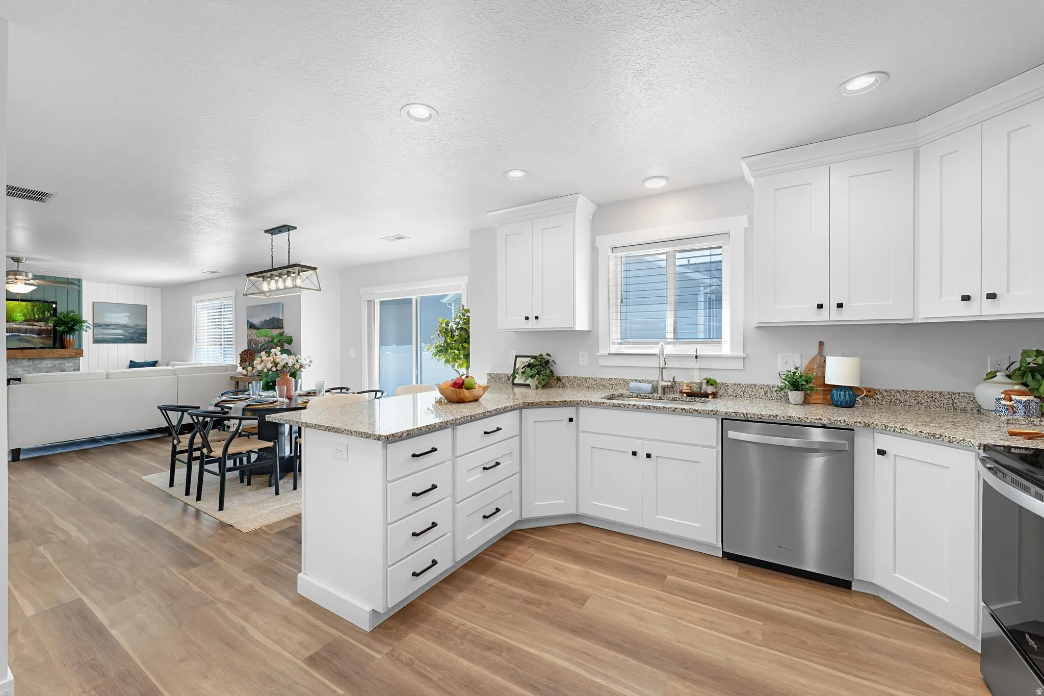 Kitchen with stainless steel appliances, light stone countertops, white cabinets, open floor plan, and a textured ceiling