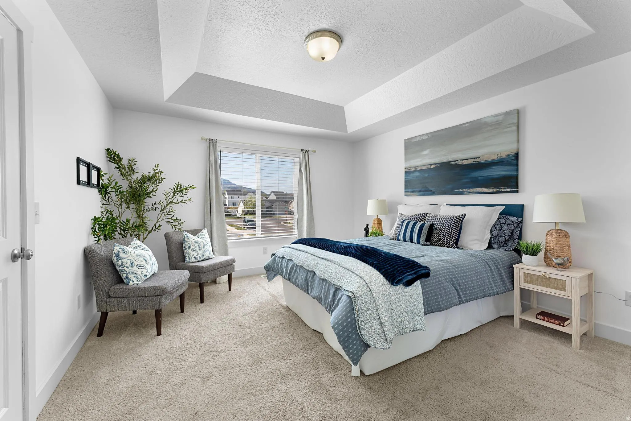 Primary bedroom with light carpet, a textured ceiling, and a tray ceiling