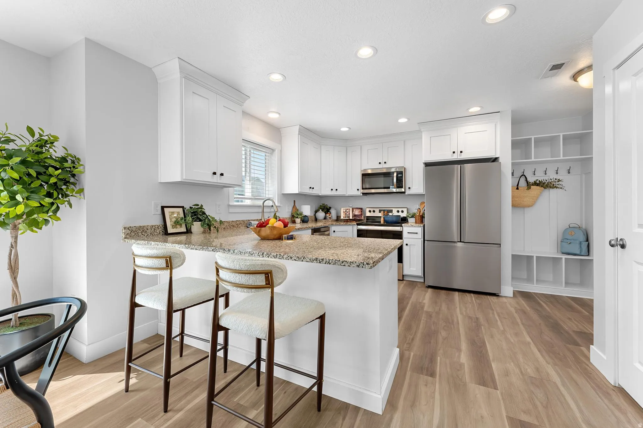 Kitchen featuring stainless steel appliances, light stone countertops, a peninsula, a breakfast bar area, and white cabinets
