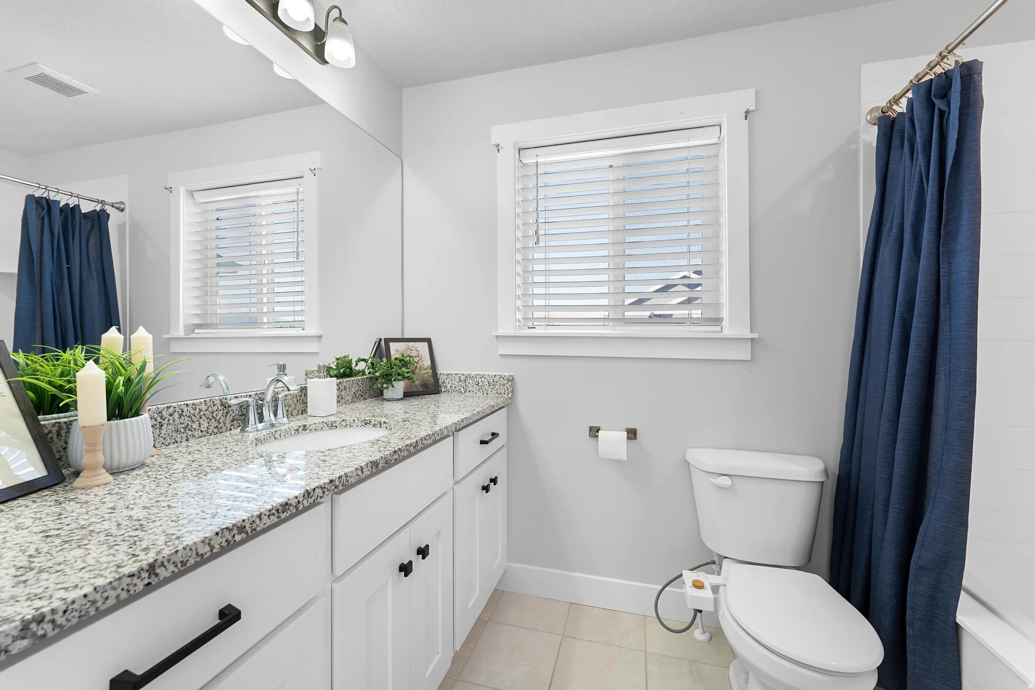 Primary suite bathroom featuring vanity, light tile patterned floors, shower / bath combo with shower curtain, and plenty of natural light