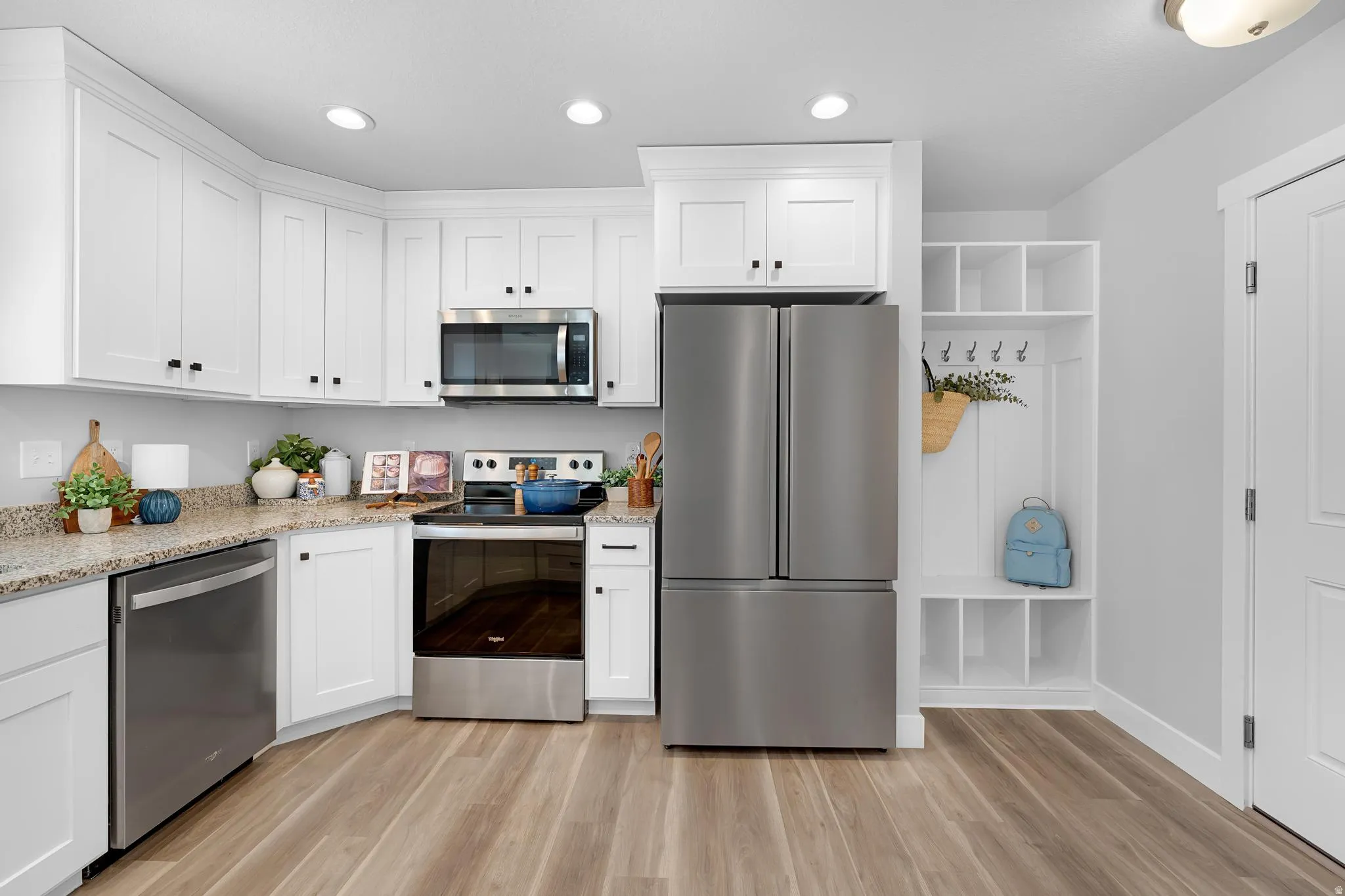 Kitchen with stainless steel appliances, white cabinetry, light stone counters, light wood finished floors, and recessed lighting