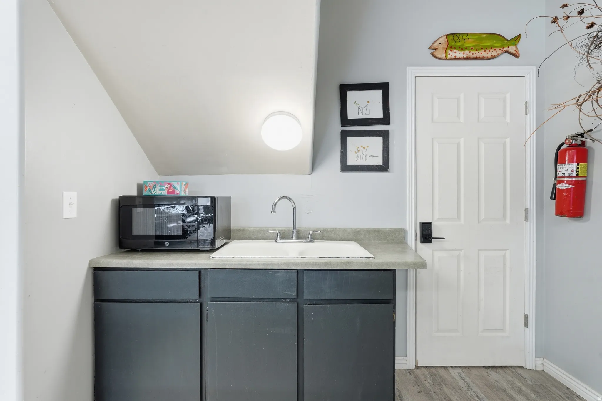 Bar featuring light countertops, black microwave, gray cabinets, wood finished floors, and lofted ceiling