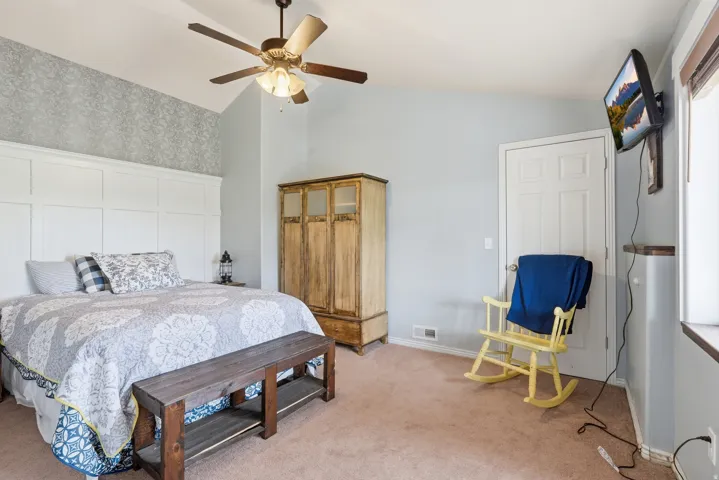 Bedroom featuring wallpapered walls, vaulted ceiling, a ceiling fan, and light colored carpet