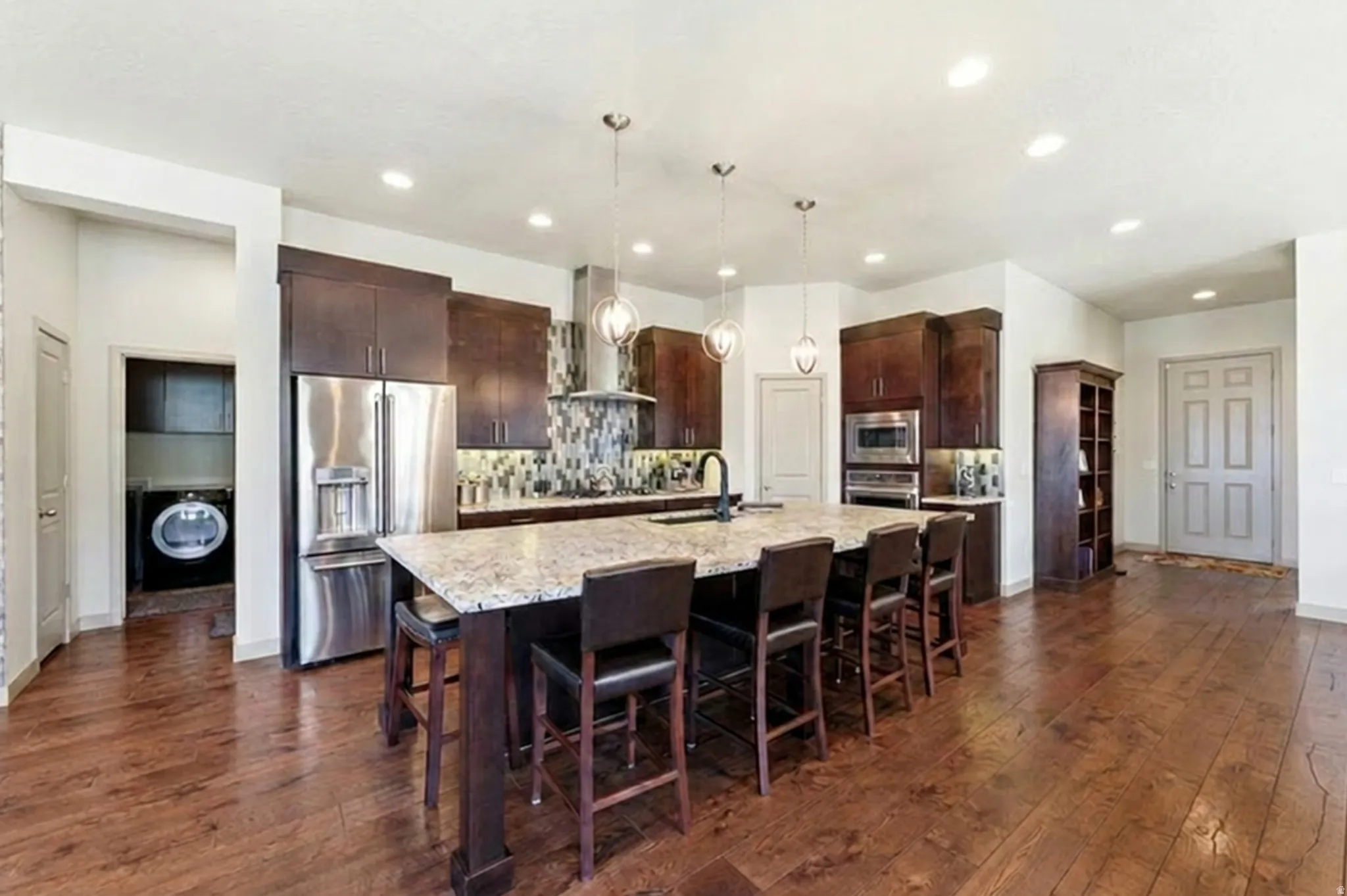 Kitchen with massive island, stainless steel appliances, real hardwood floors, dark wood cabinetry, decorative backsplash and granite counter tops.