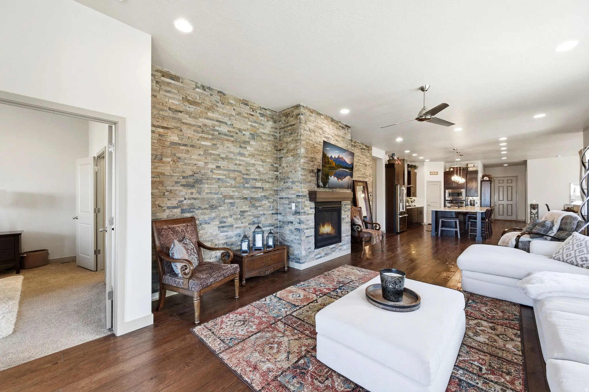 Living room with hardwood flooring, a fireplace, a ceiling fan, and door to primary bedroom.