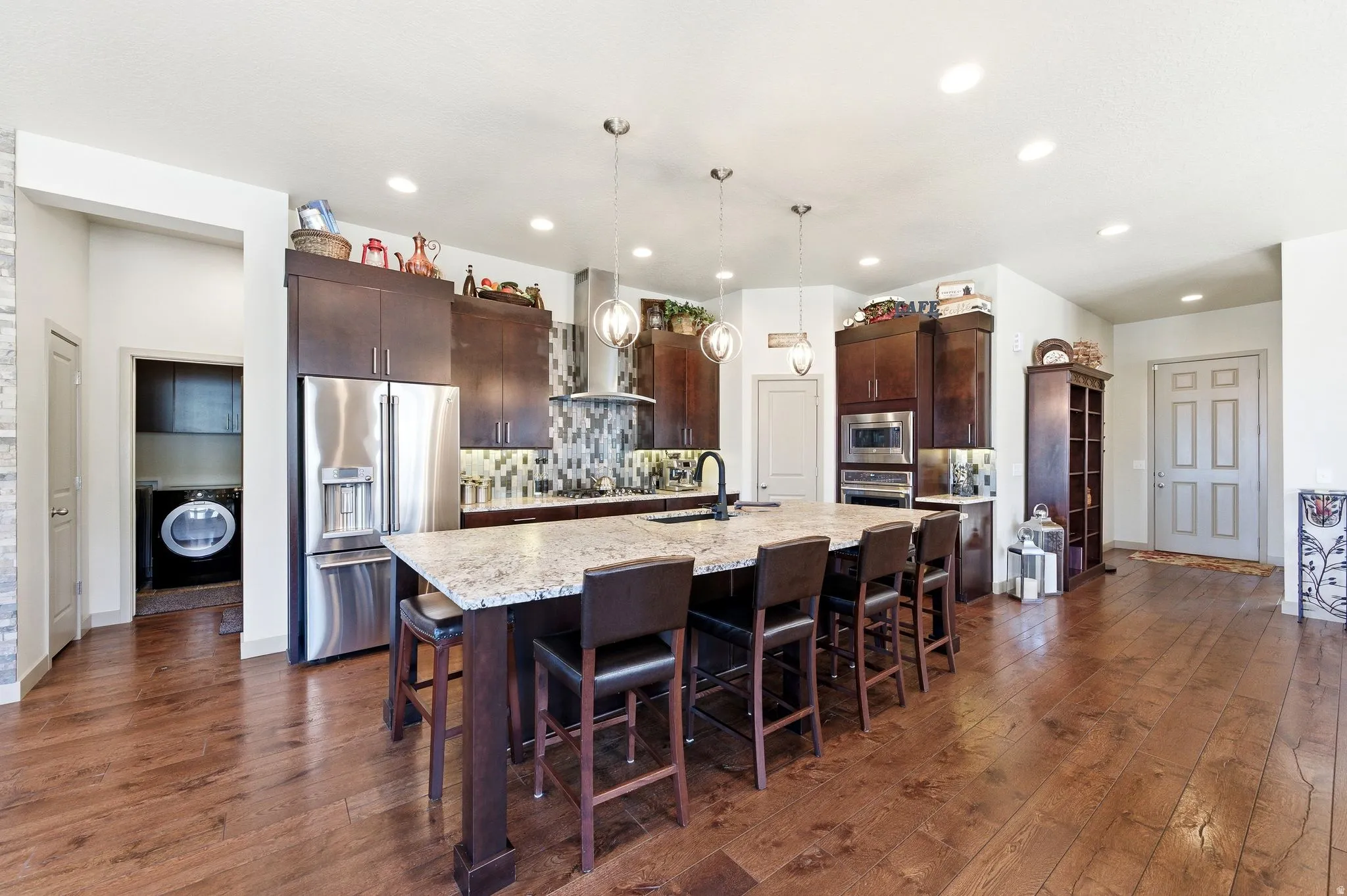 Kitchen with massive island, stainless steel appliances, real hardwood floors, dark wood cabinetry, decorative backsplash and granite counter tops.