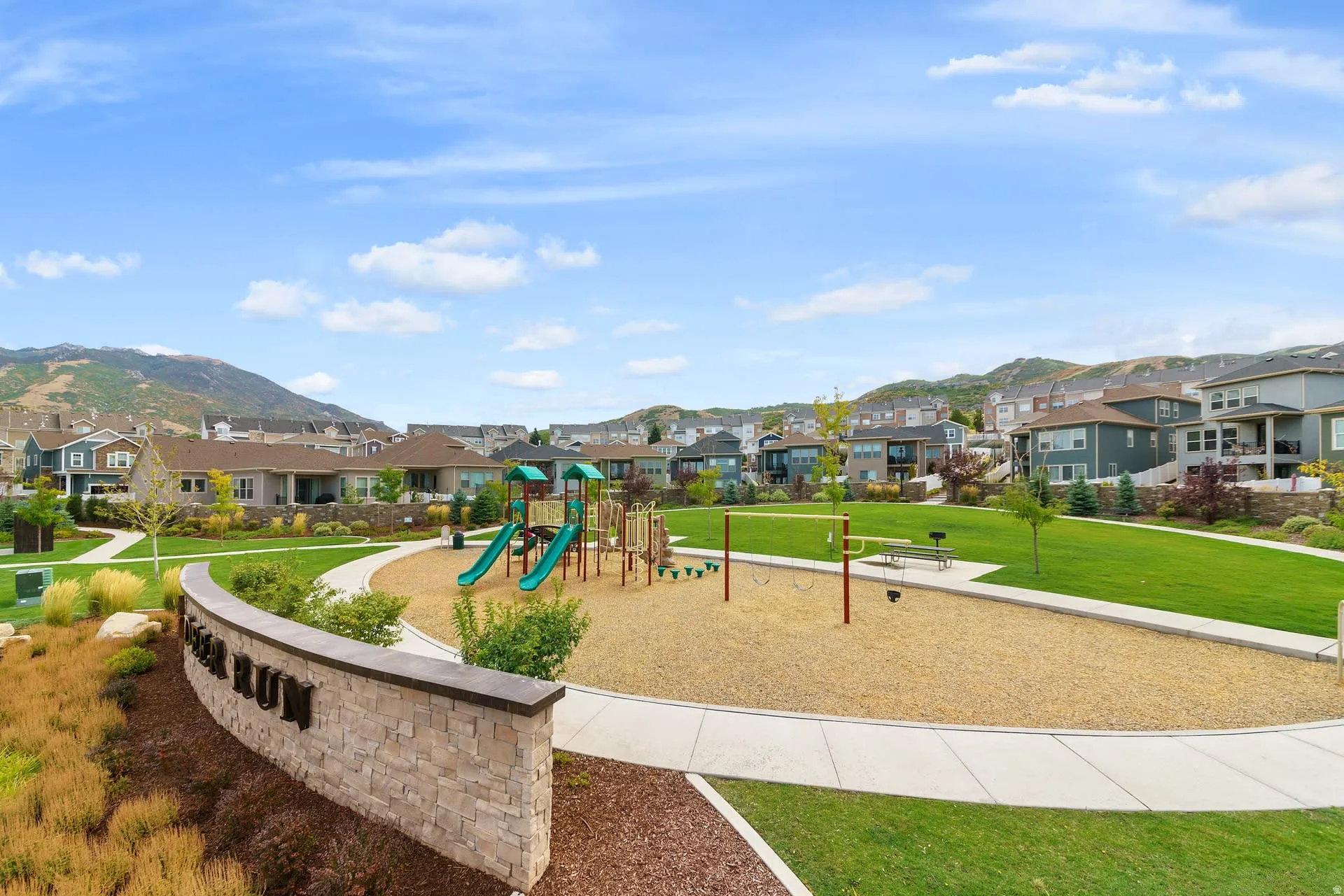 Community park with play structures, open green space, paved walkways, and mountain backdrop
