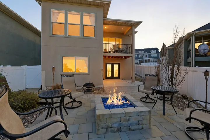 Back of house at dusk with french doors, a balcony, stucco siding, a fenced backyard with fire pit