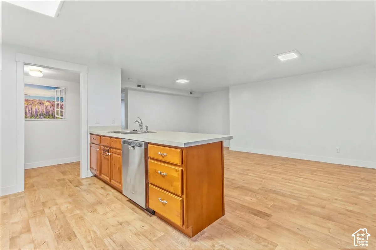 Kitchen featuring light countertops, a peninsula, wood finish cabinetry, light wood-style floors, and stainless steel dishwasher