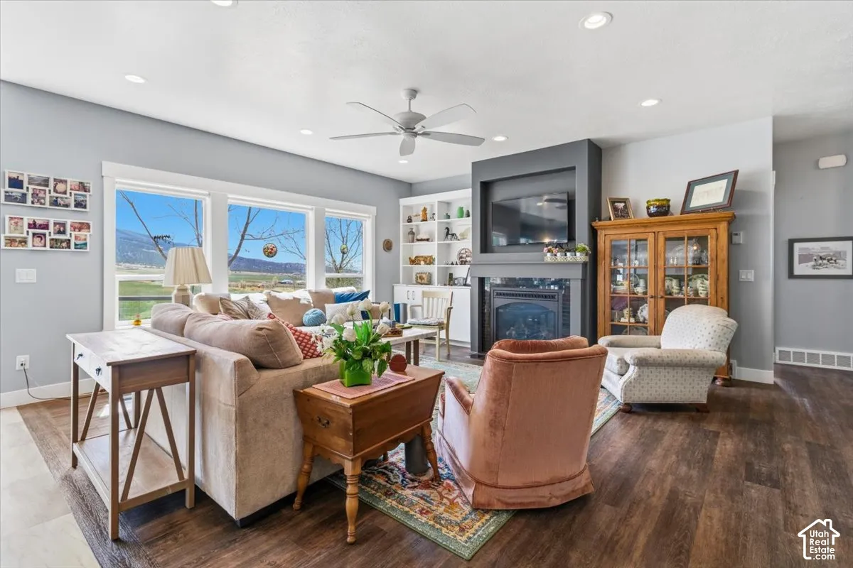 Living room featuring a glass covered fireplace, wood finished floors, a ceiling fan, and recessed lighting
