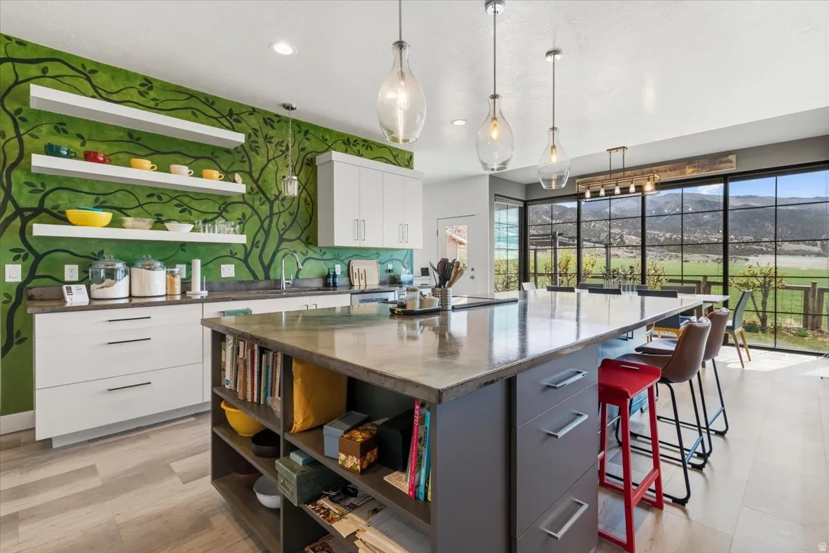 Kitchen featuring open shelves, hanging light fixtures, two tone cabinets, a large island, and dark stone countertops