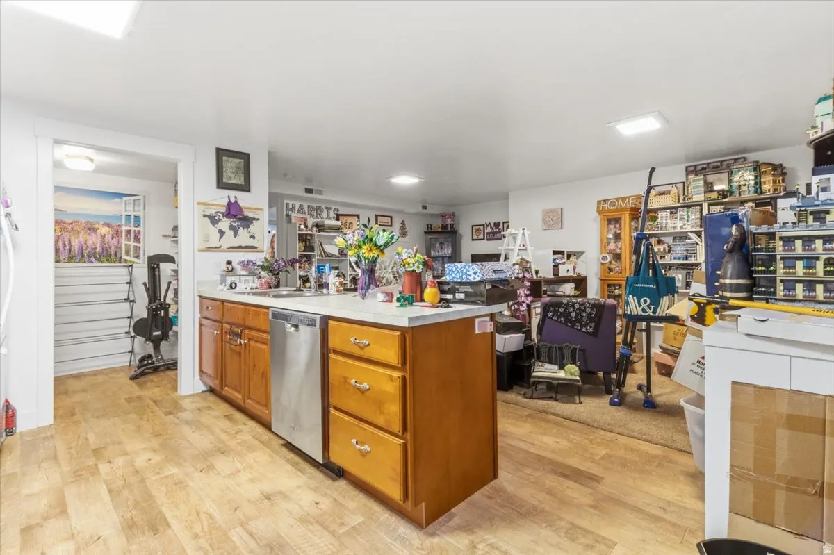Kitchen featuring light countertops, wood finish cabinetry, a peninsula, light wood-style floors, and stainless steel dishwasher