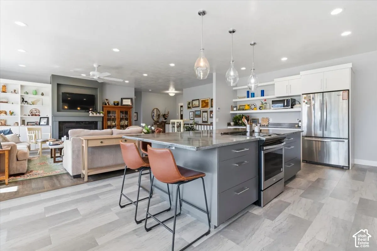 Kitchen featuring a spacious island, a breakfast bar, stainless steel appliances, dual tone cabinets, and a fireplace