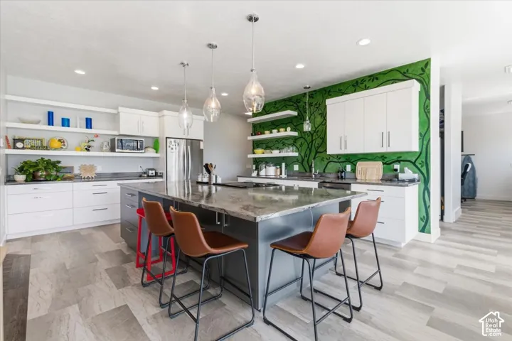 Kitchen featuring open shelves, a breakfast bar area, stainless steel appliances, hanging light fixtures, and two tone color scheme