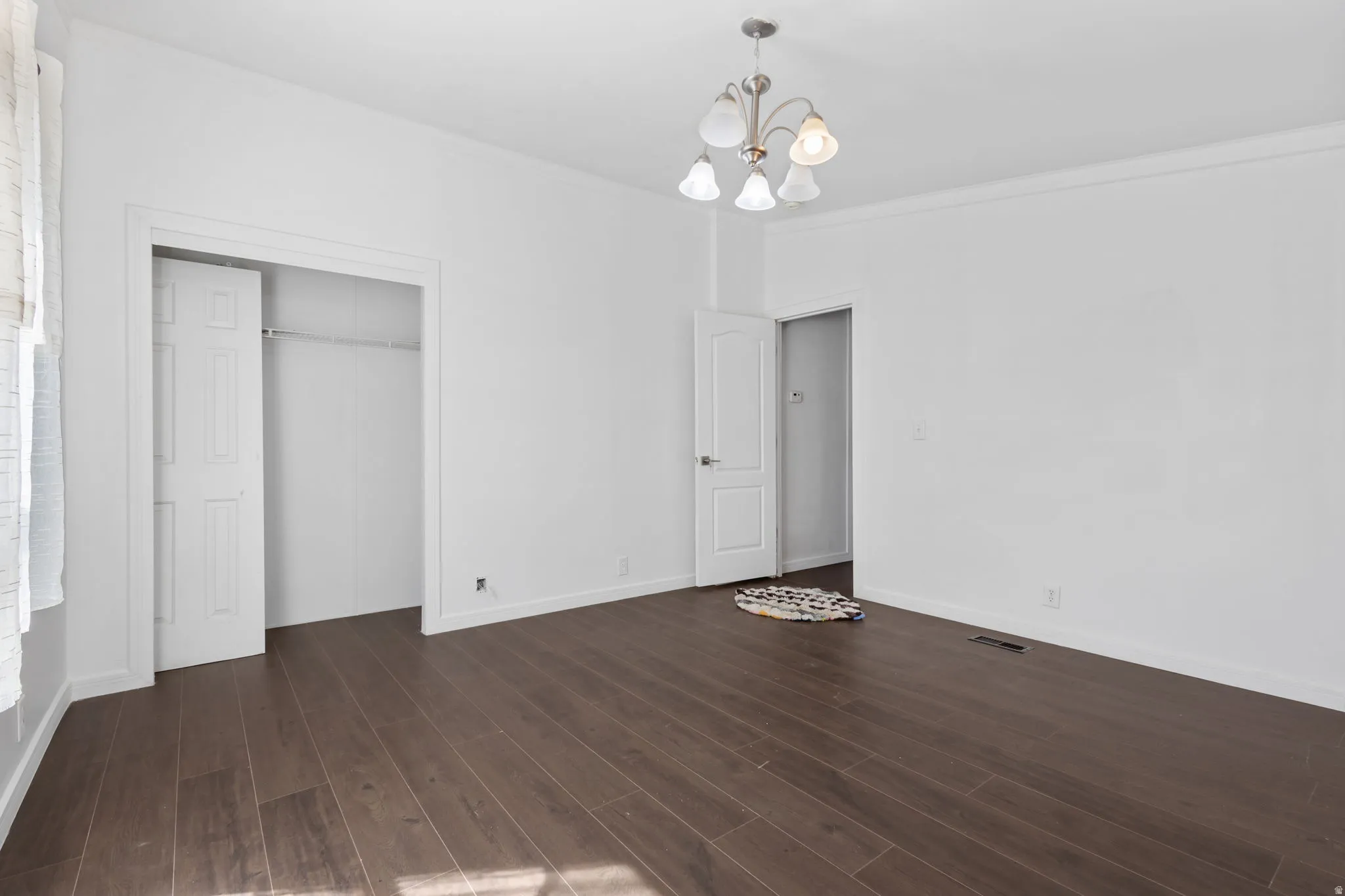 Unfurnished bedroom featuring crown molding, a closet, a chandelier, and dark wood-style flooring