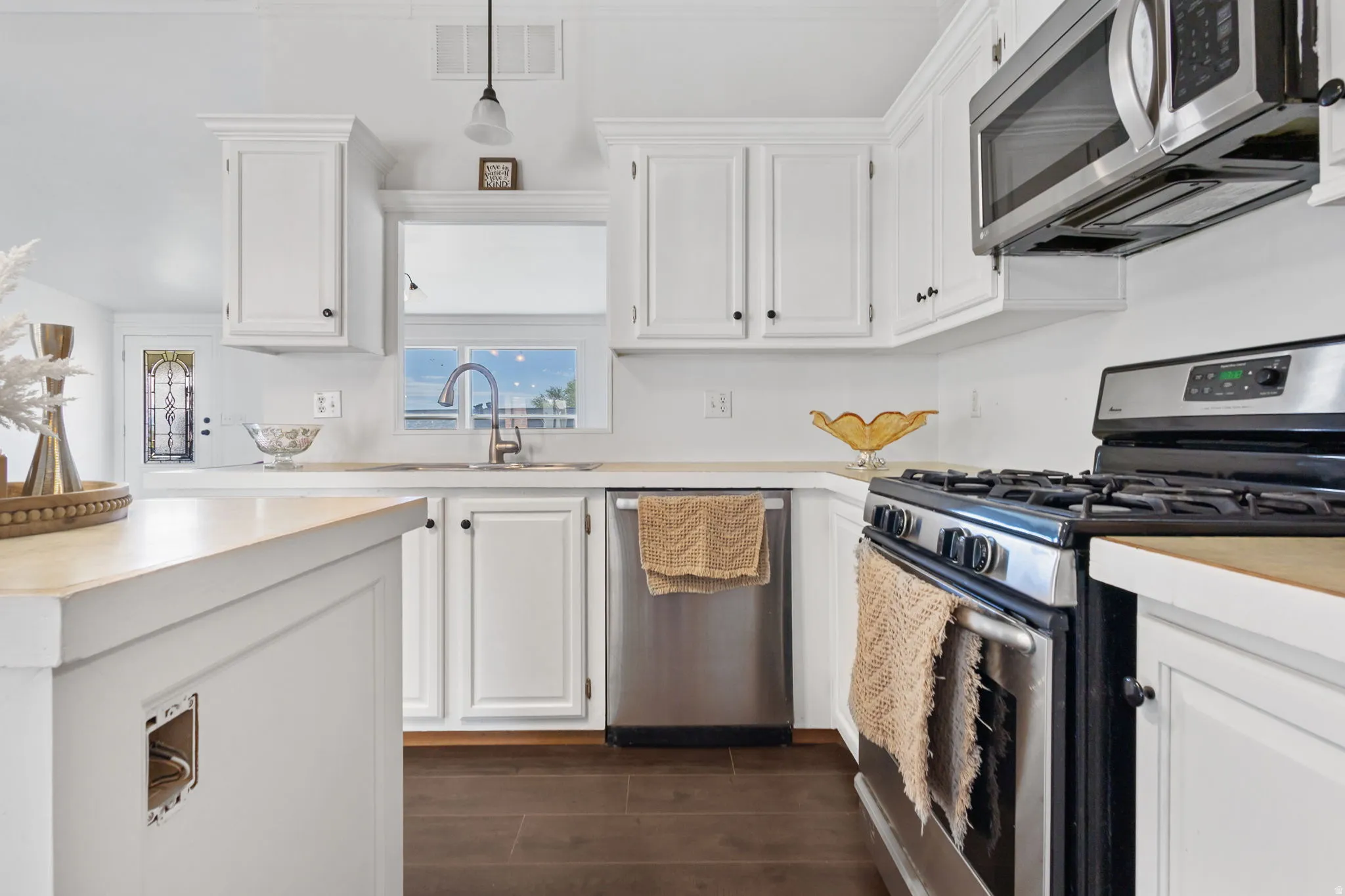 Kitchen with stainless steel appliances, light countertops, white cabinetry, and dark wood-style flooring