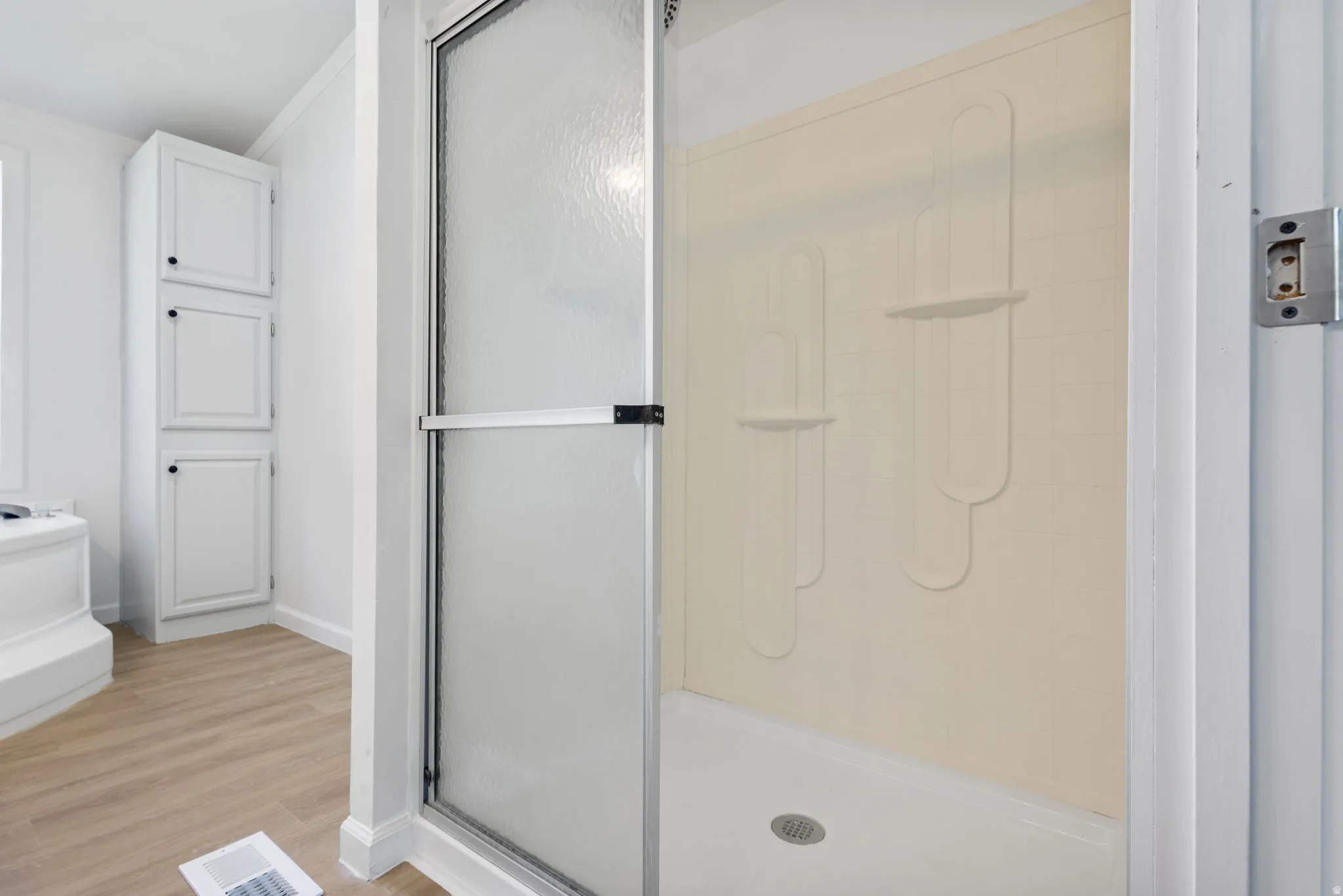 Bathroom with light wood-style flooring, a shower stall, and ornamental molding