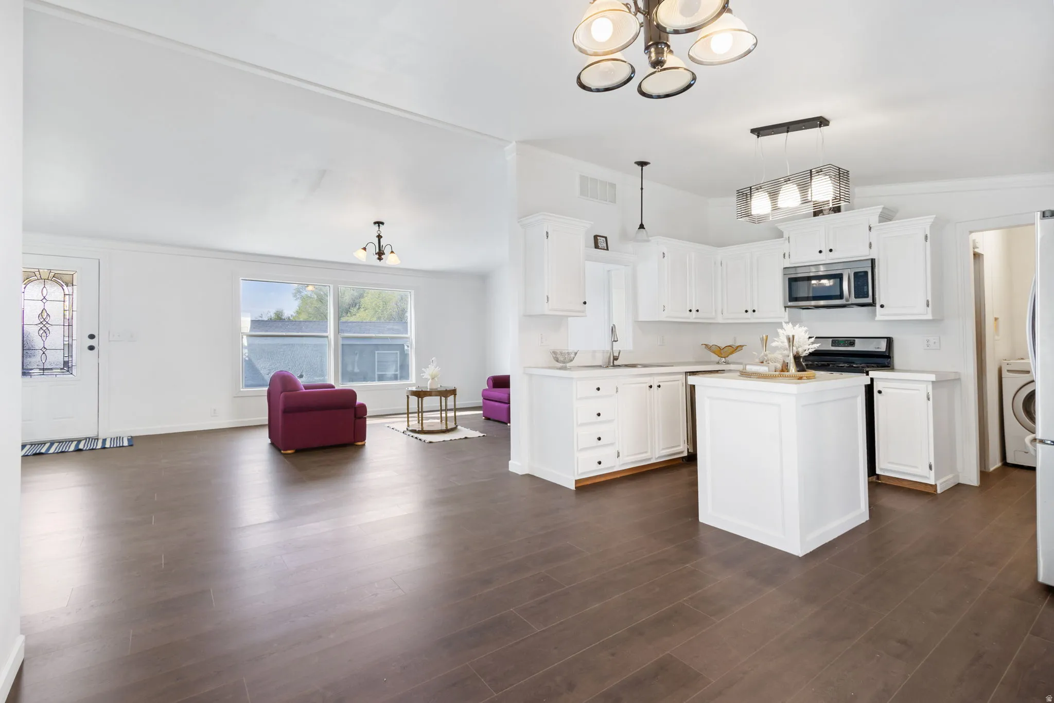 Kitchen featuring suspended lighting, light countertops, a kitchen island, white cabinetry, and ornamental molding