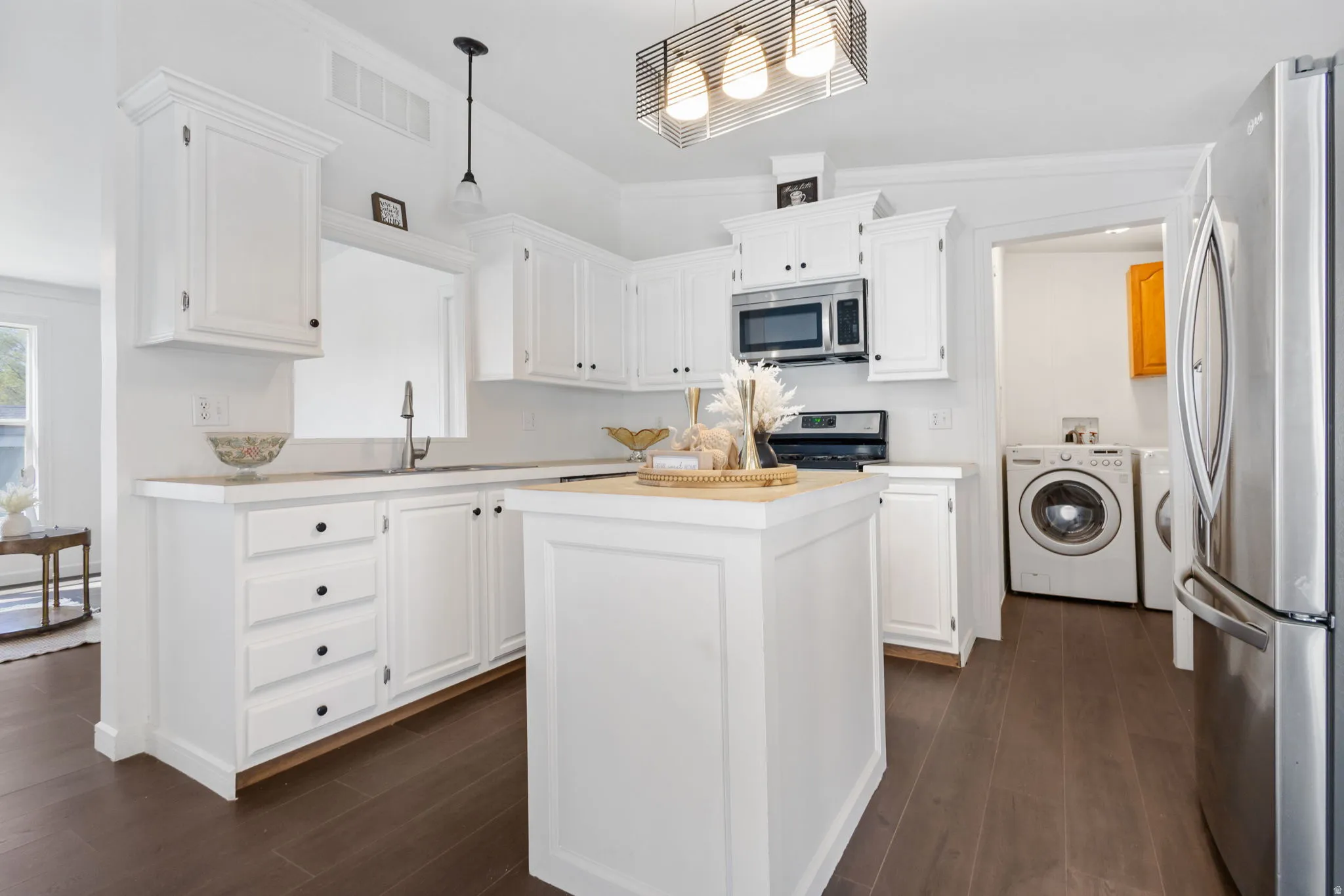 Kitchen with stainless steel appliances, a center island, white cabinets, pendant lighting, and ornamental molding