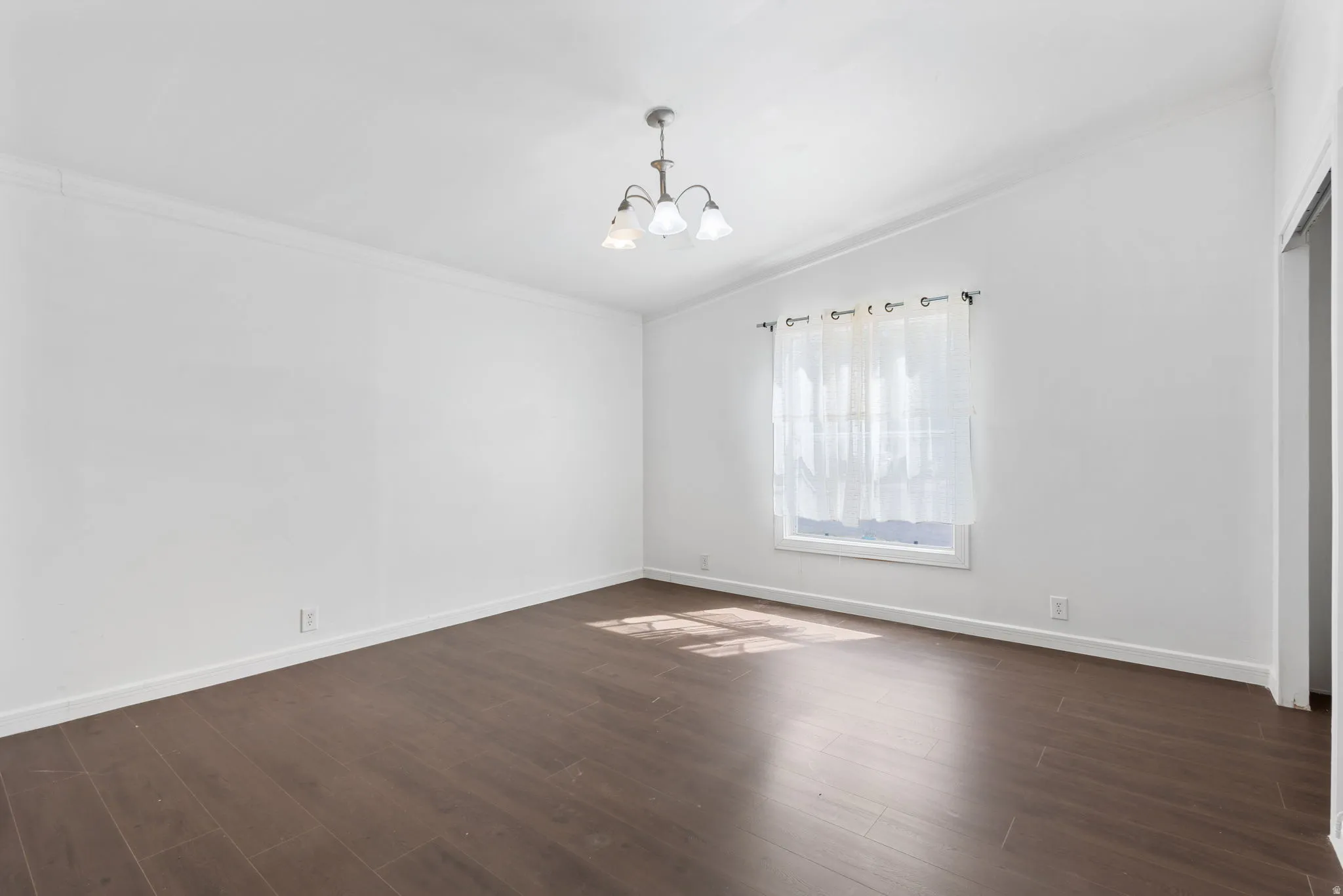 Spare room with lofted ceiling, hanging lights, dark wood-style flooring, and ornamental molding