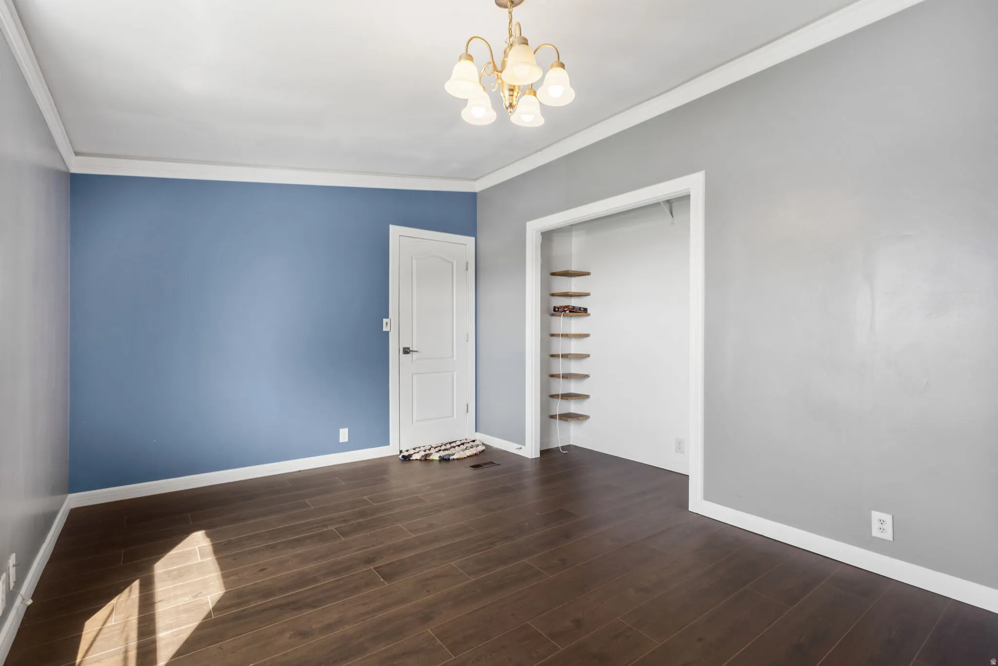 Spare room featuring ornamental molding, dark wood-type flooring, and a chandelier