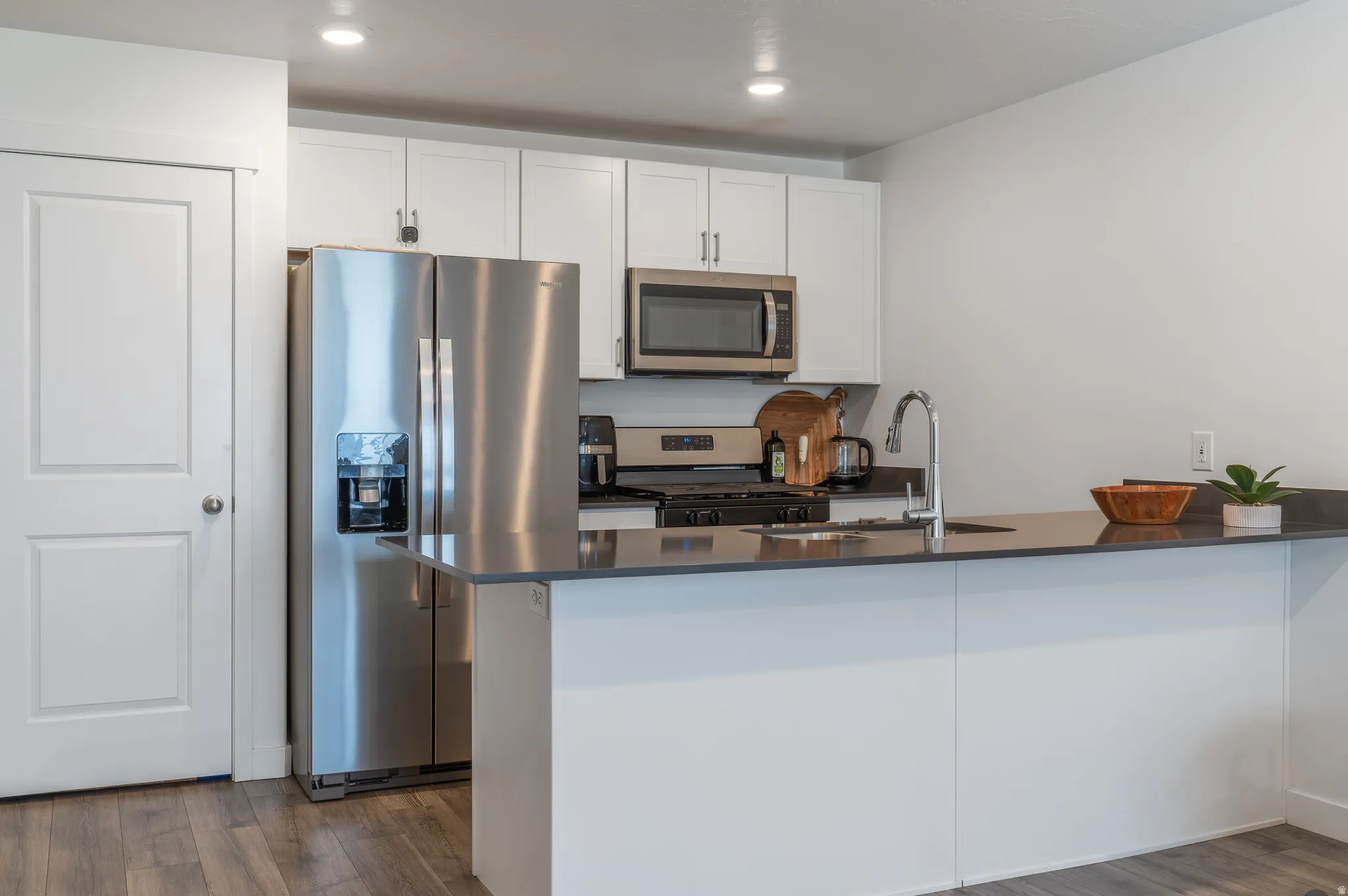 Kitchen featuring stainless steel appliances, white cabinets, a peninsula, dark wood-type flooring, and recessed lighting