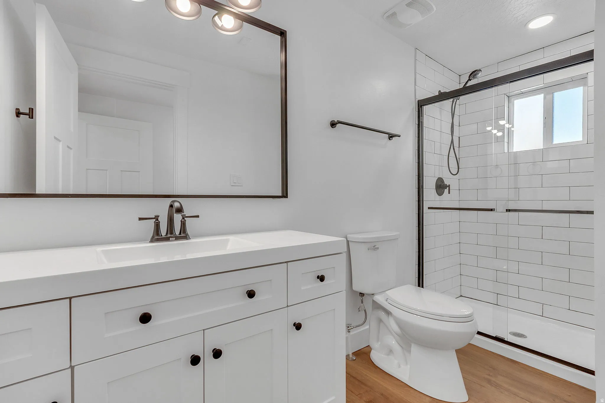 Master bathroom with vanity, a subway-tiled shower, and light wood LVP floors