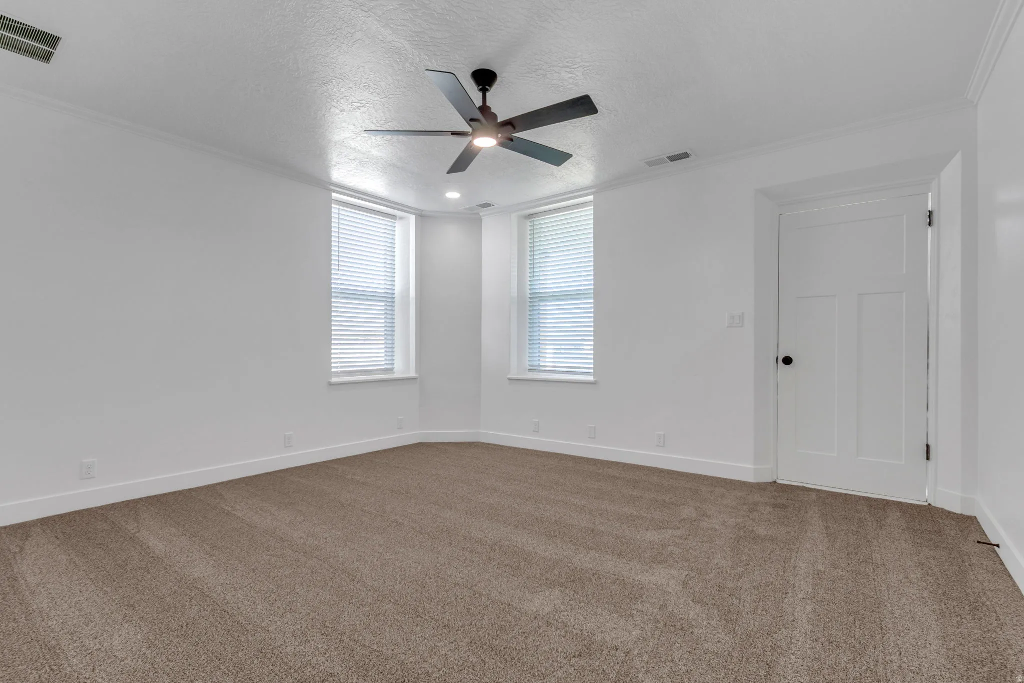 Mater bedroom featuring dark colored carpet, a ceiling fan, crown molding, and a private entrance.
