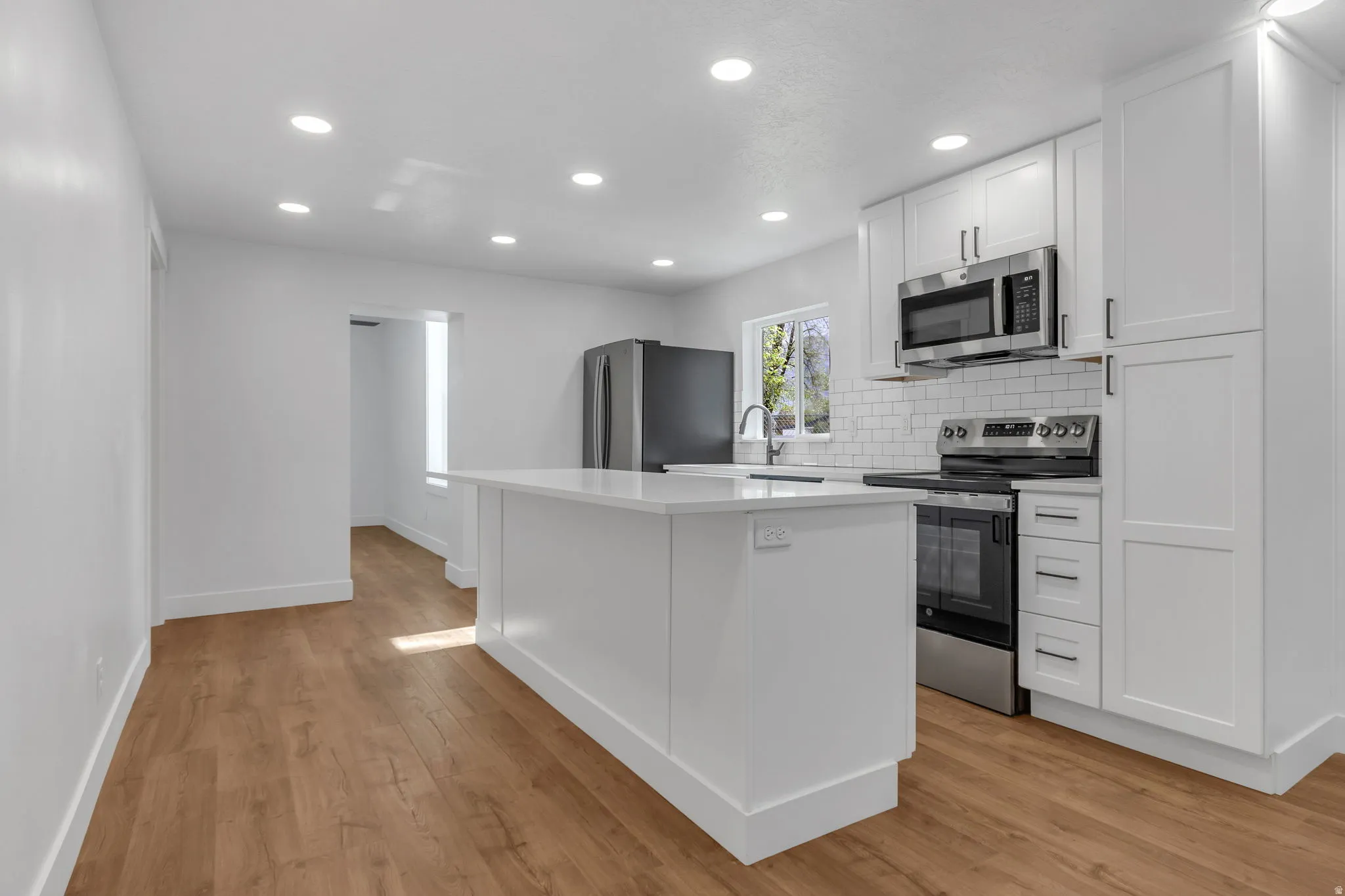 Kitchen with white shaker cabinets, stainless steel appliances, backsplash, recessed lighting, and light wood LVP finished flooring, and