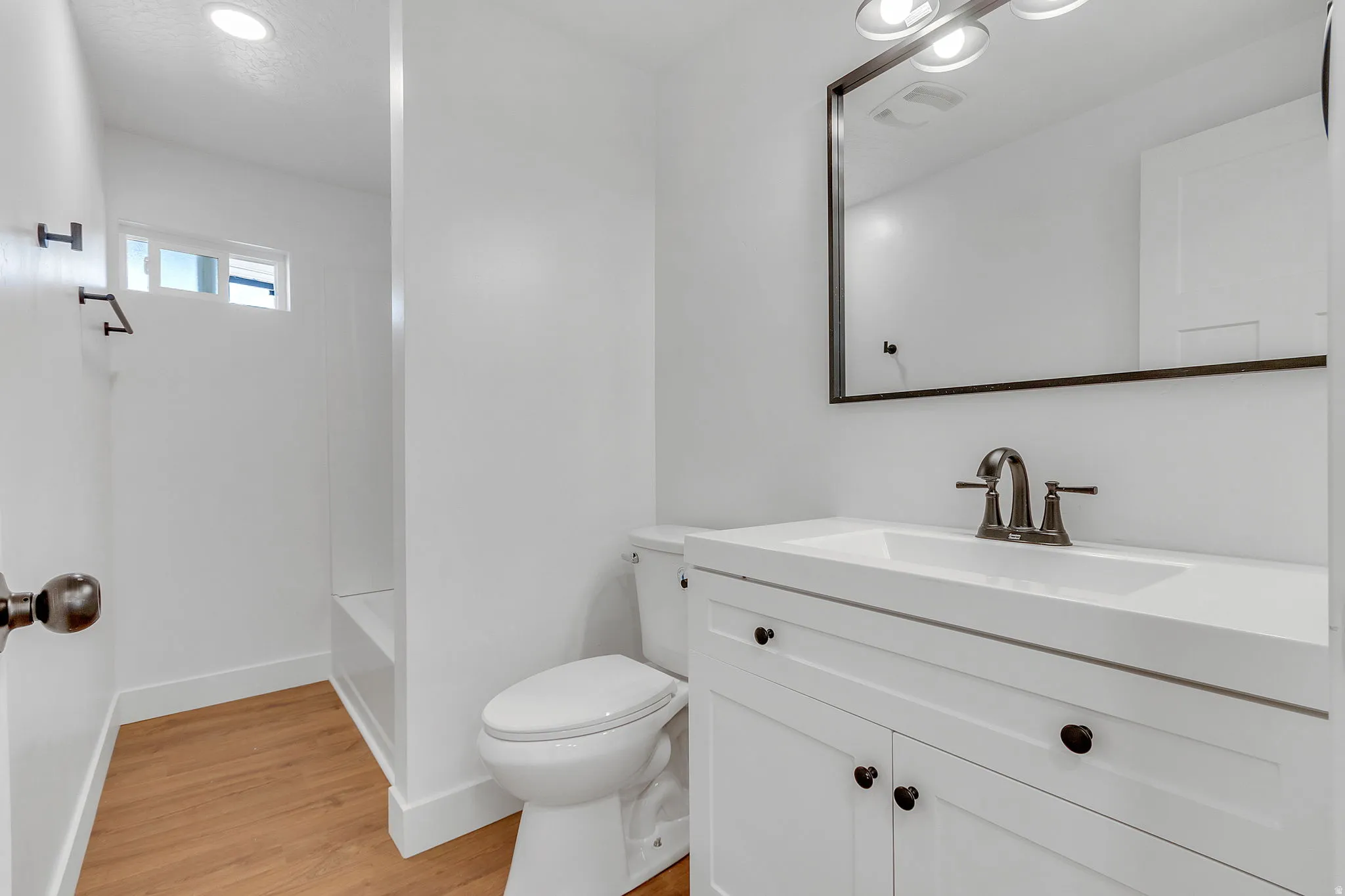 Bathroom featuring vanity, light wood LVP floors, a shower, and recessed lighting