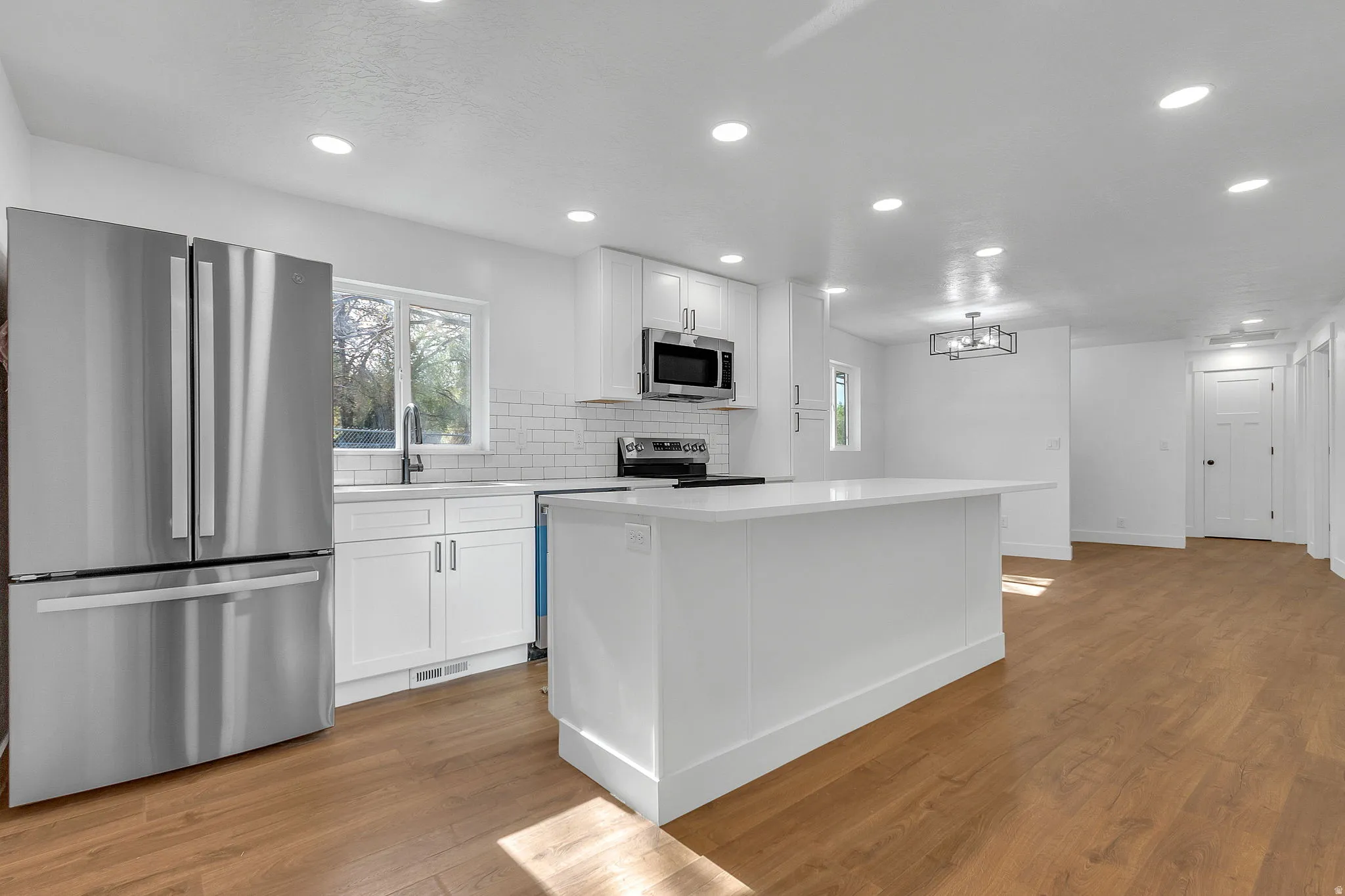 Kitchen with stainless steel appliances, light wood LVP floors, white shaker cabinetry, a quartz center island, and plenty of natural light.