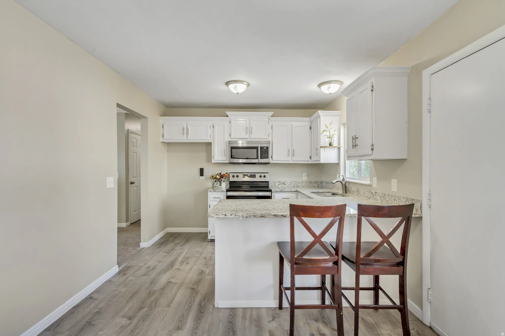Kitchen featuring a kitchen bar, stainless steel appliances, white cabinetry, a peninsula, and light wood finished floors