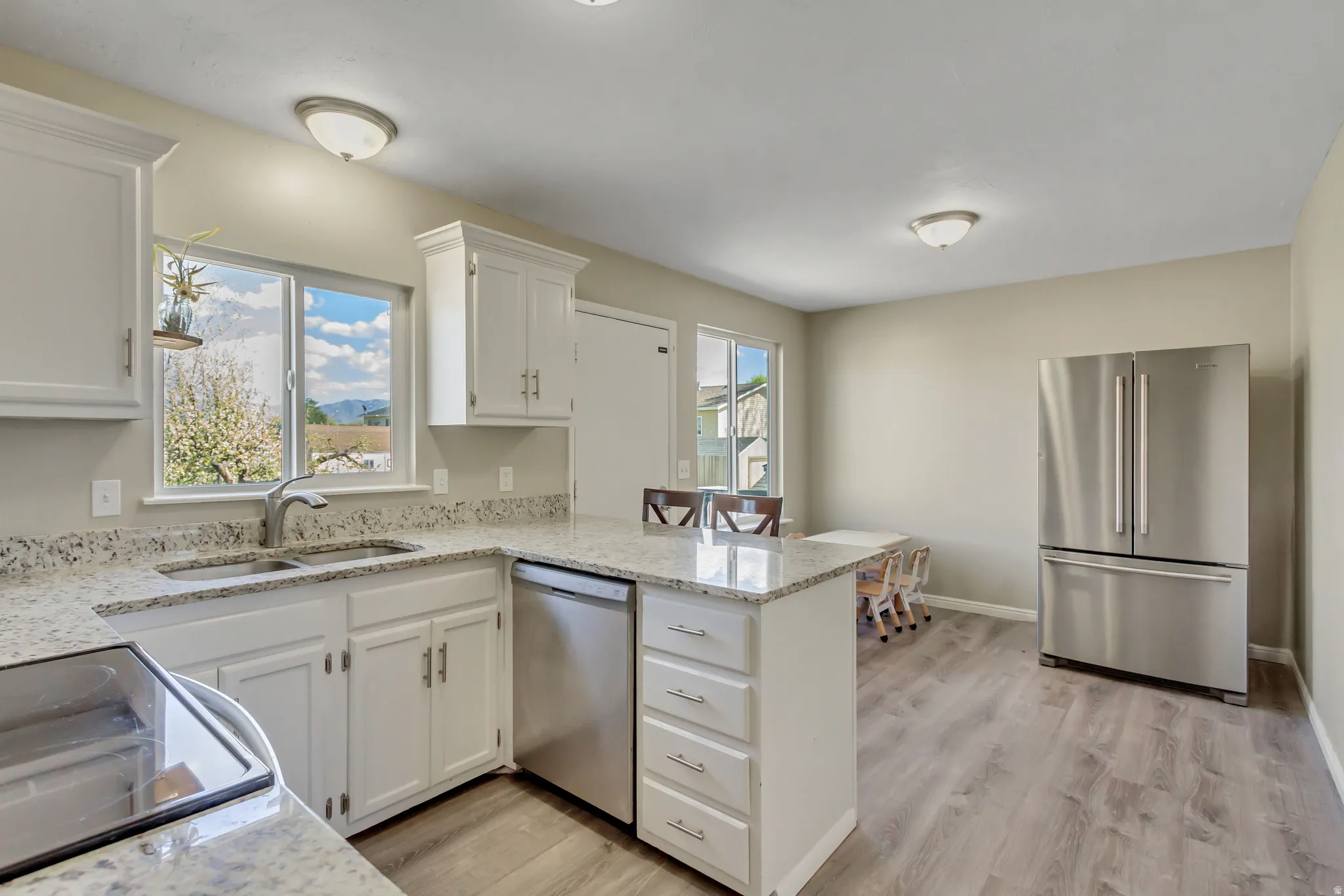 Kitchen with stainless steel appliances, white cabinetry, light wood finished floors, a peninsula, and light stone counters