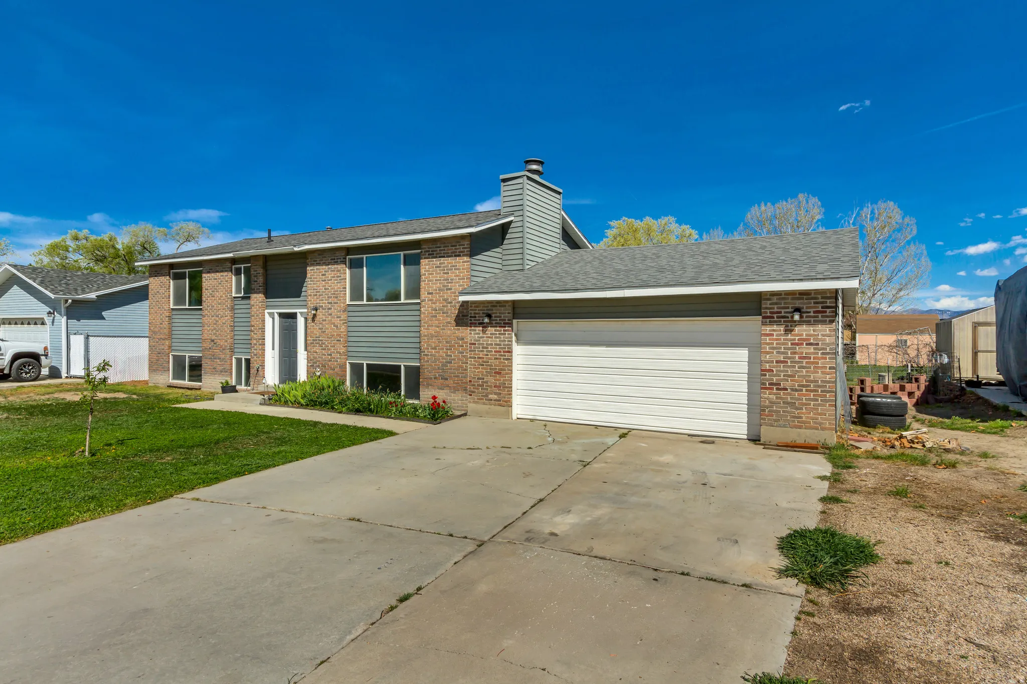 Raised ranch featuring an attached garage, driveway, brick siding, and roof with shingles