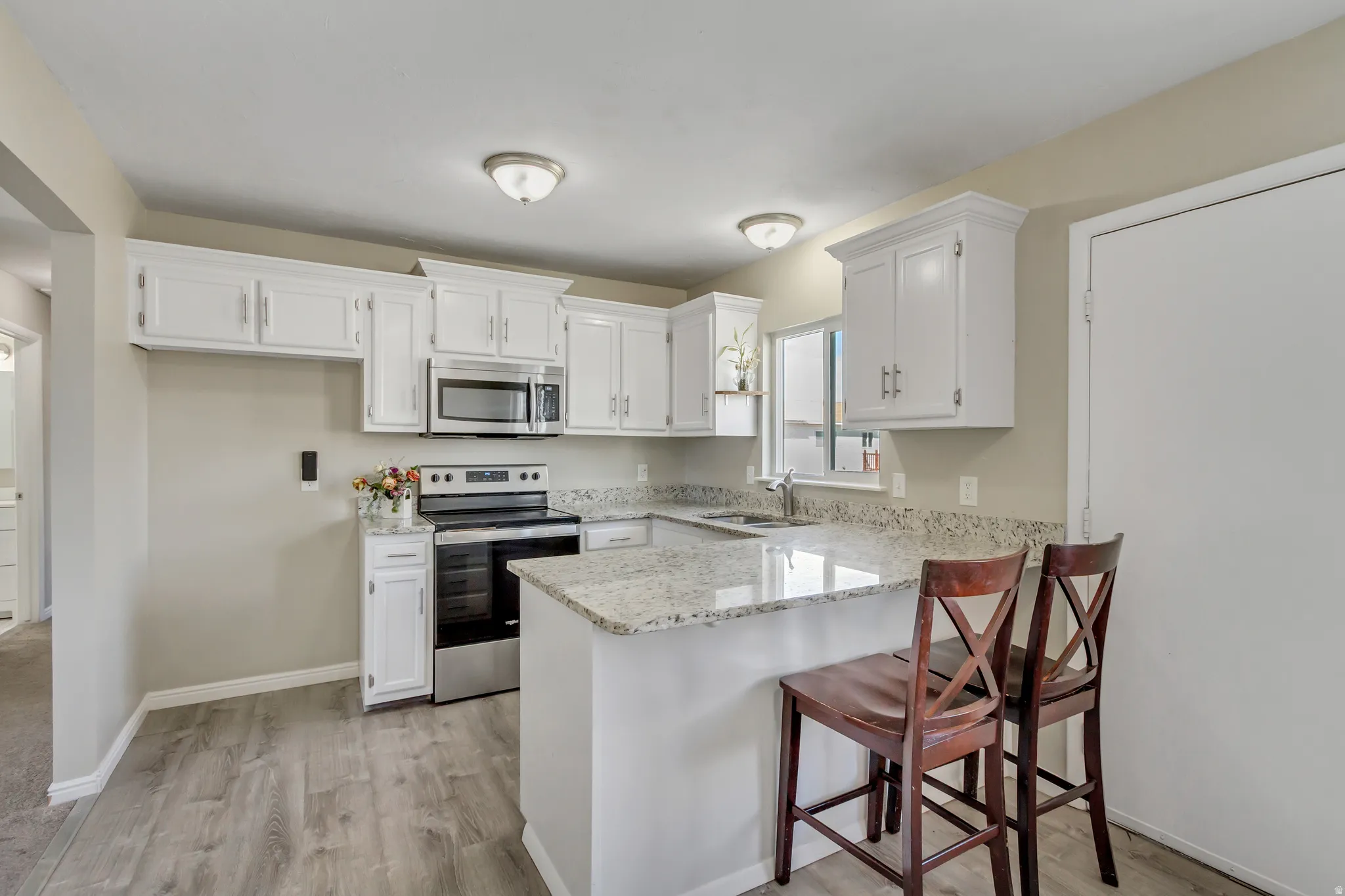 Kitchen featuring stainless steel appliances, a kitchen breakfast bar, white cabinets, light stone counters, and a peninsula