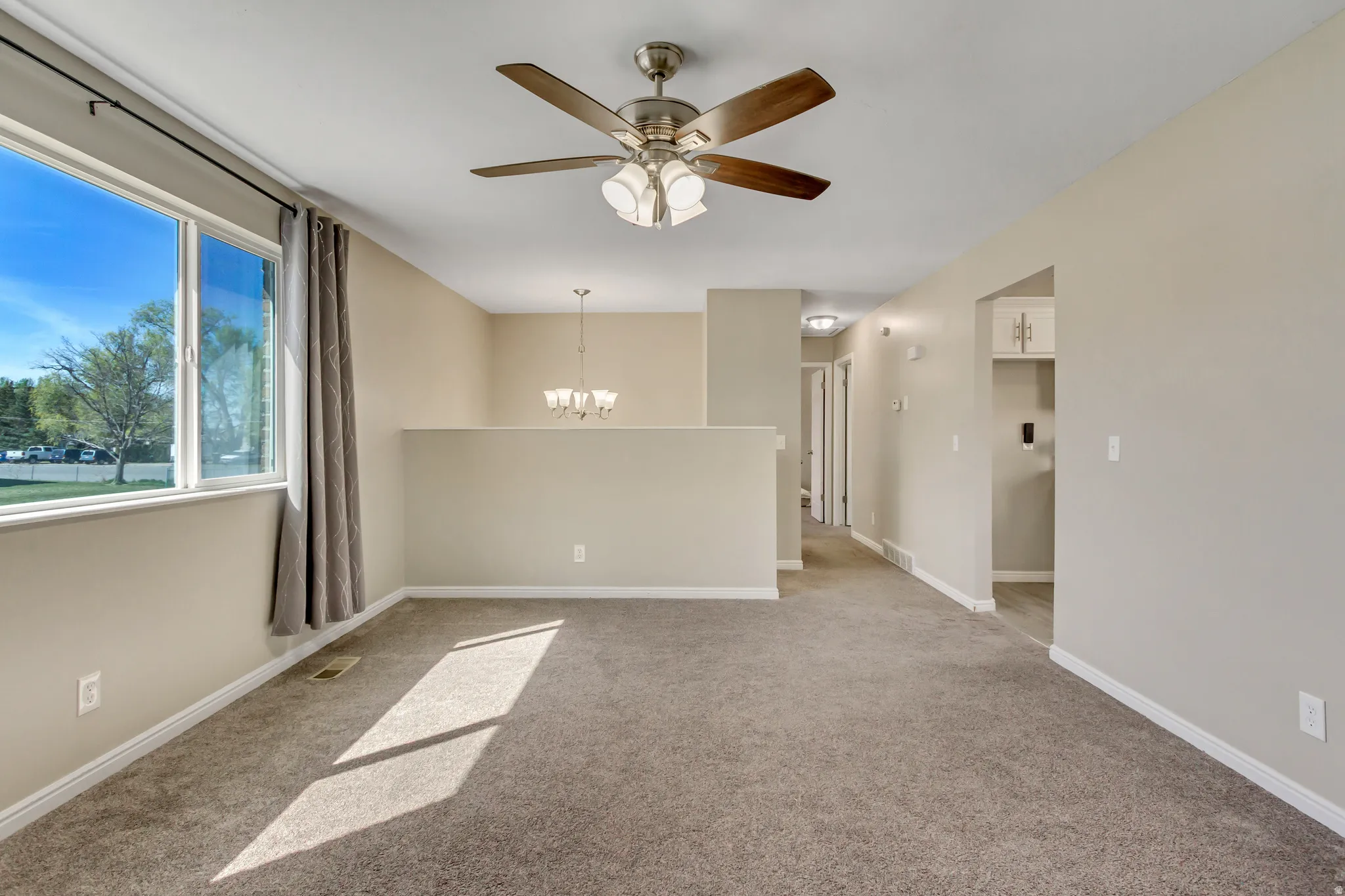 Empty room featuring a ceiling fan, light carpet, and a chandelier