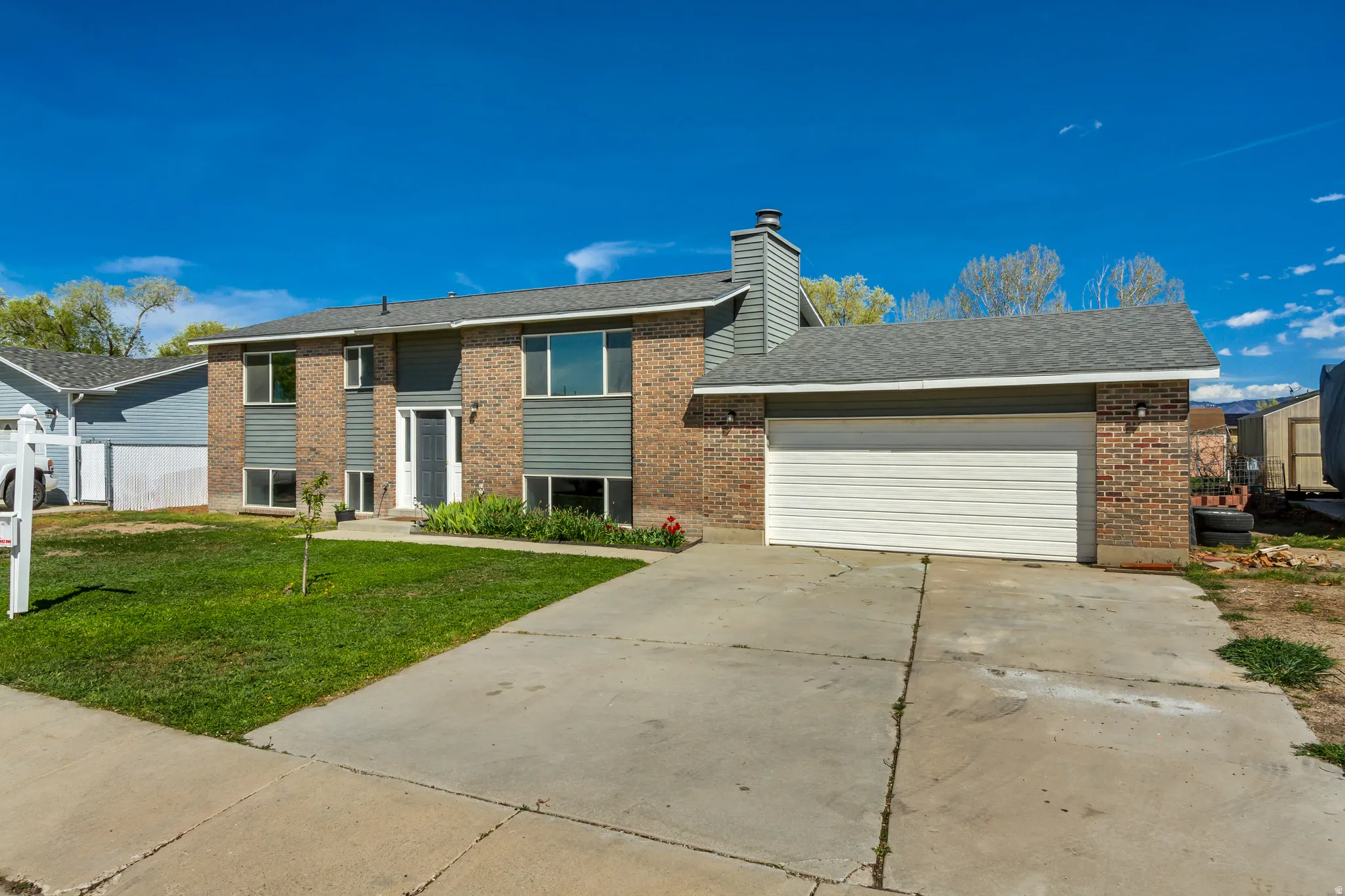 Raised ranch with a front lawn, an attached garage, driveway, brick siding, and a chimney