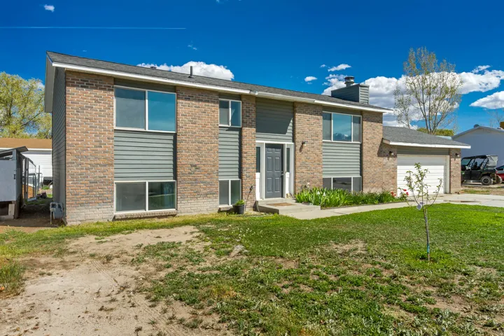 Raised ranch with an attached garage, brick siding, a front lawn, and a chimney