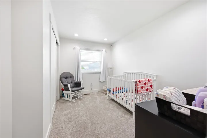 Bedroom featuring light colored carpet, a crib, and recessed lighting