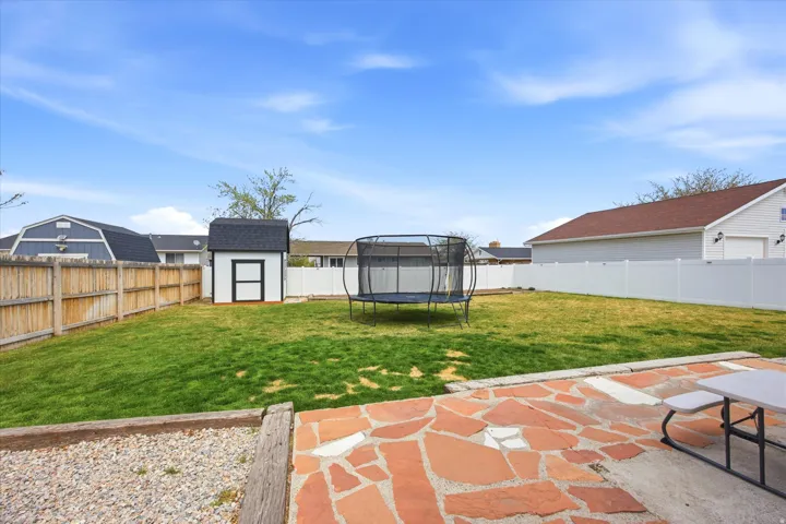 Fenced backyard with a shed, a trampoline, and a patio area