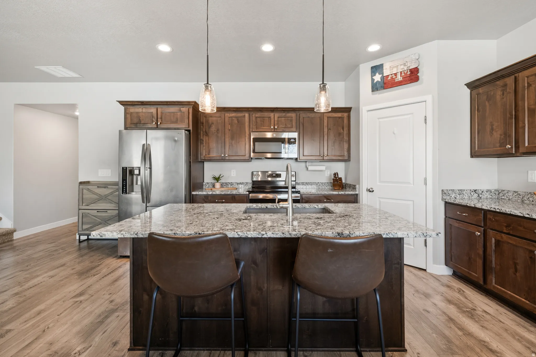 Kitchen featuring granite counters, wood cabinetry, stainless steel appliances, and a kitchen island with sink