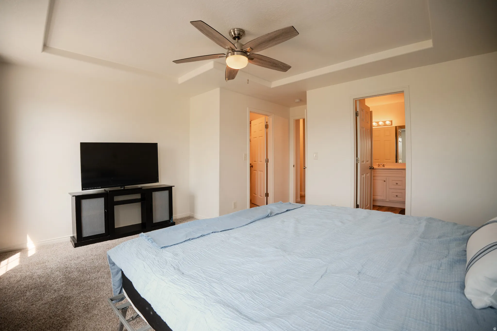 Bedroom with a raised ceiling, carpet, a ceiling fan, and ensuite bath