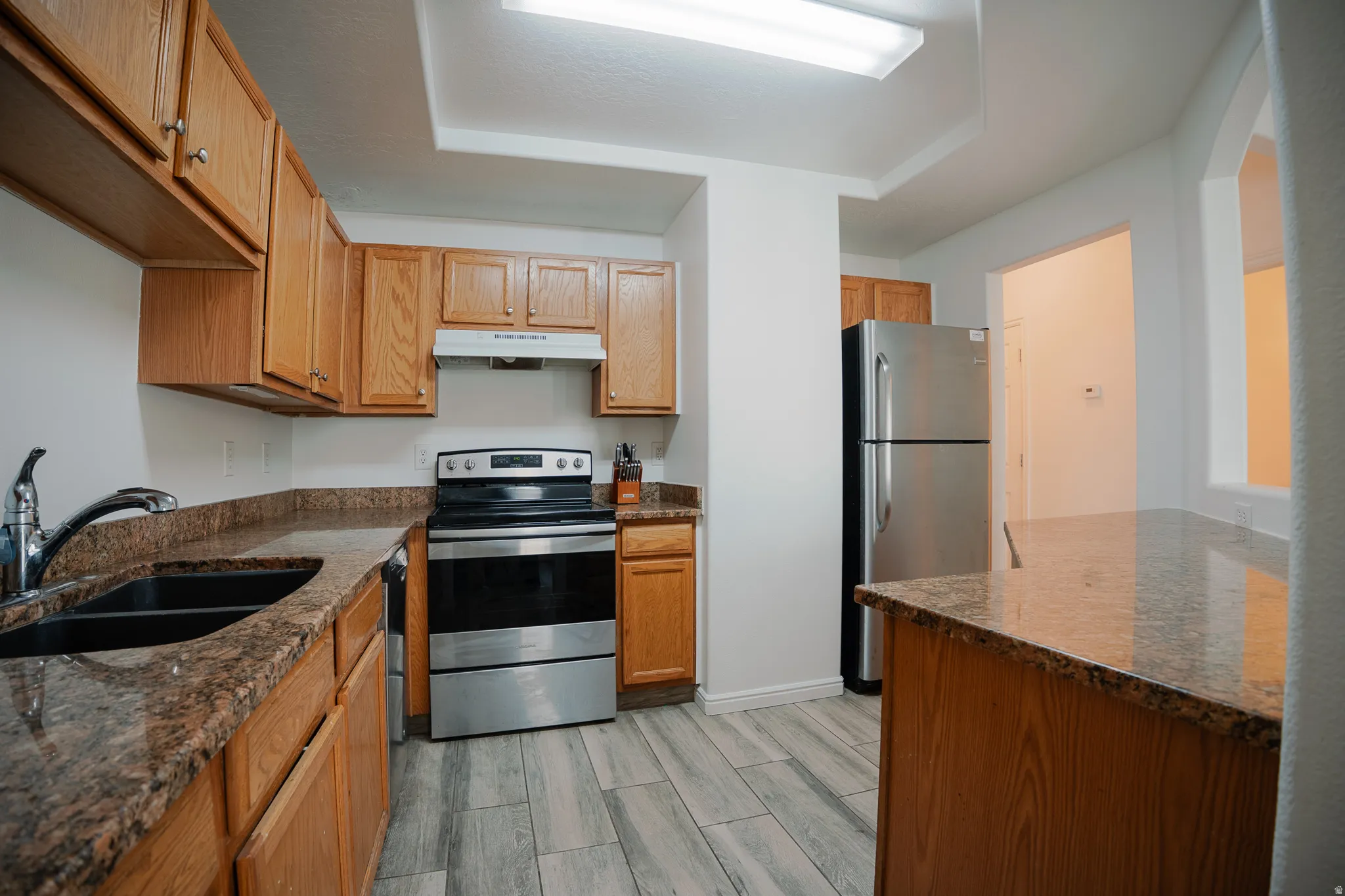 Kitchen featuring stainless steel appliances, dark stone counters, wood finish floors, and wood finish cabinetry