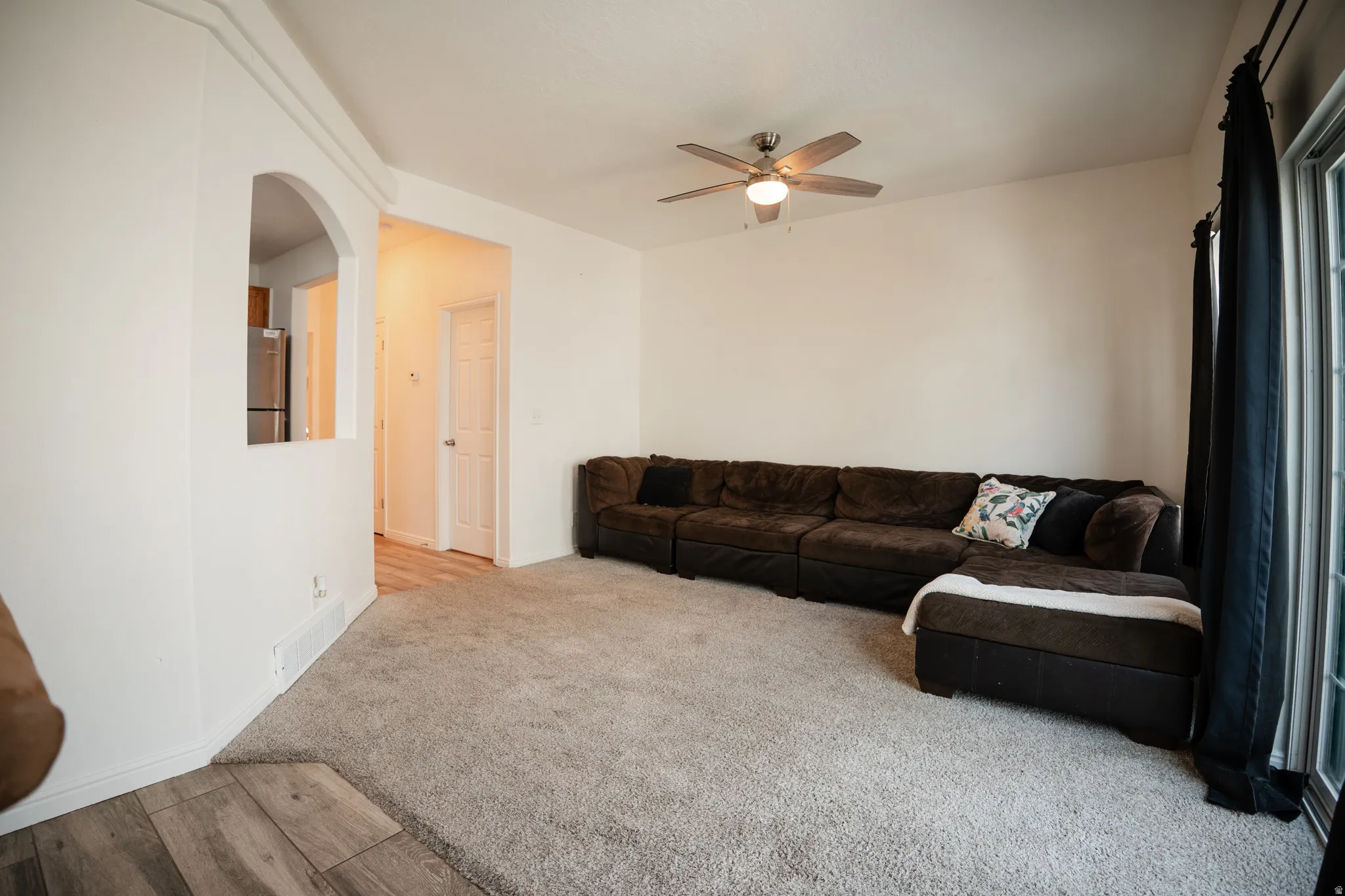 Living area featuring a ceiling fan, light colored carpet, arched walkways, and light wood-type flooring